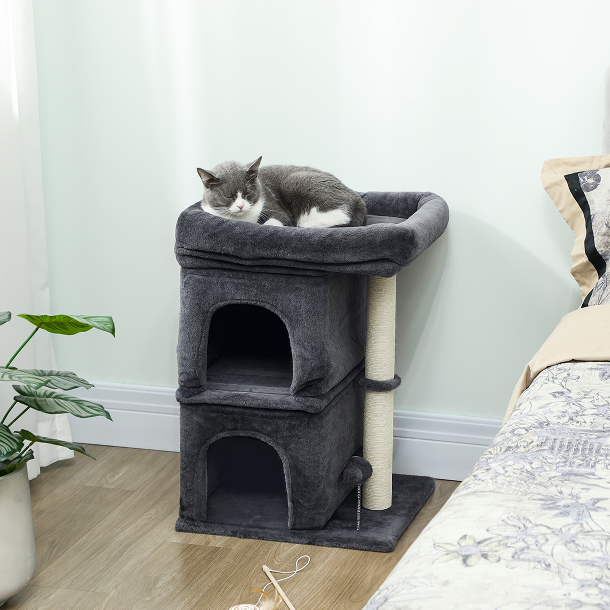 Un gato gris duerme en un árbol para gatos gris junto a una cama.
