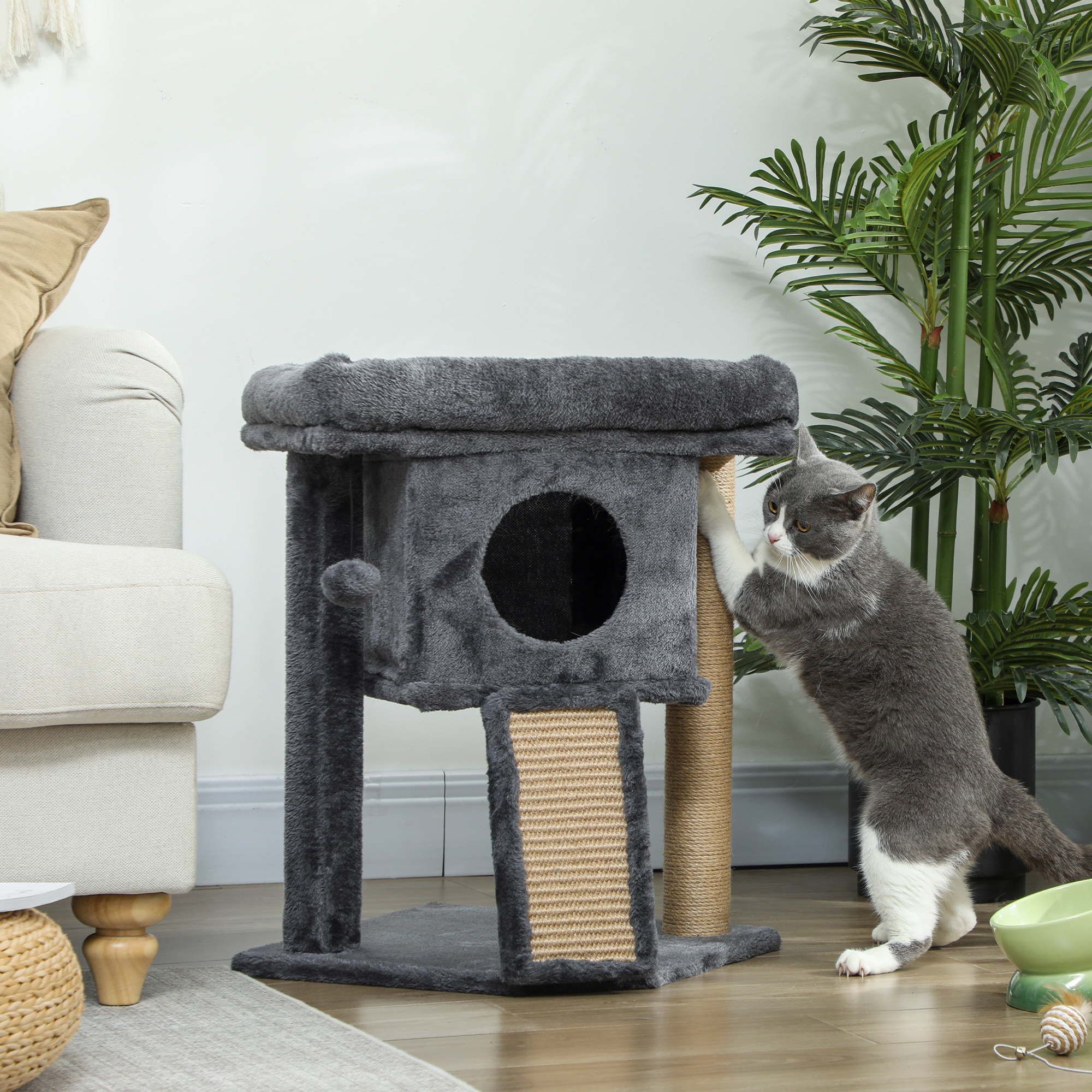 Un gato juega en un árbol para gatos junto a un sofá y una planta.