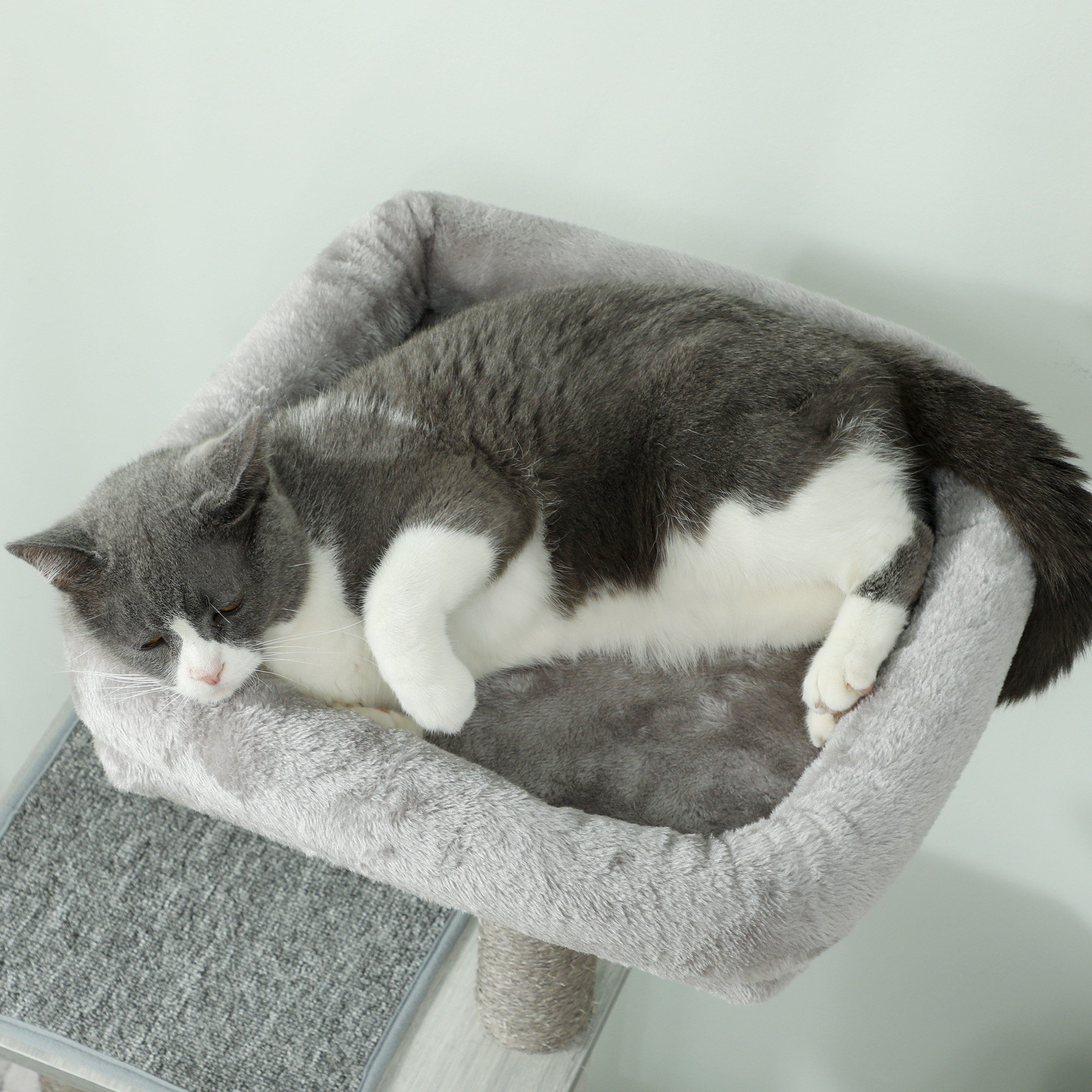 Un gato gris y blanco duerme acurrucado en una cama gris para gatos en un rascador.