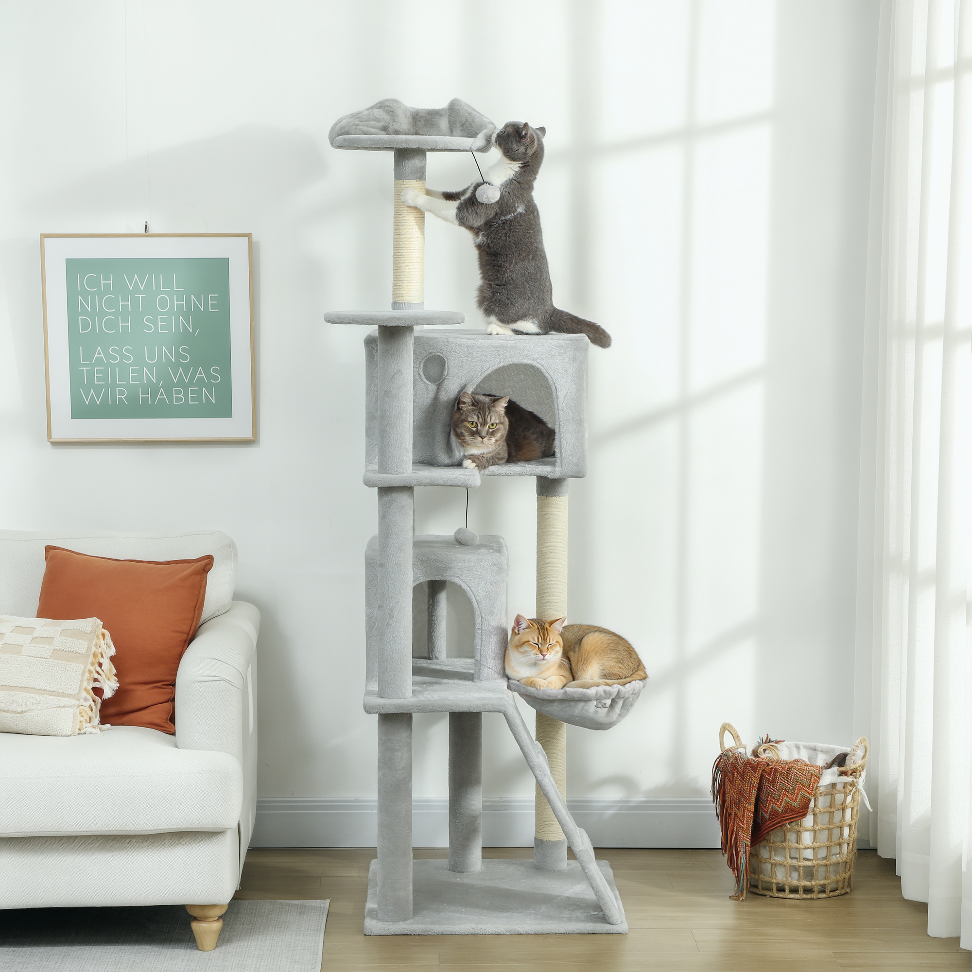 Tres gatos en un árbol para gatos en una sala con sofá y cuadro.