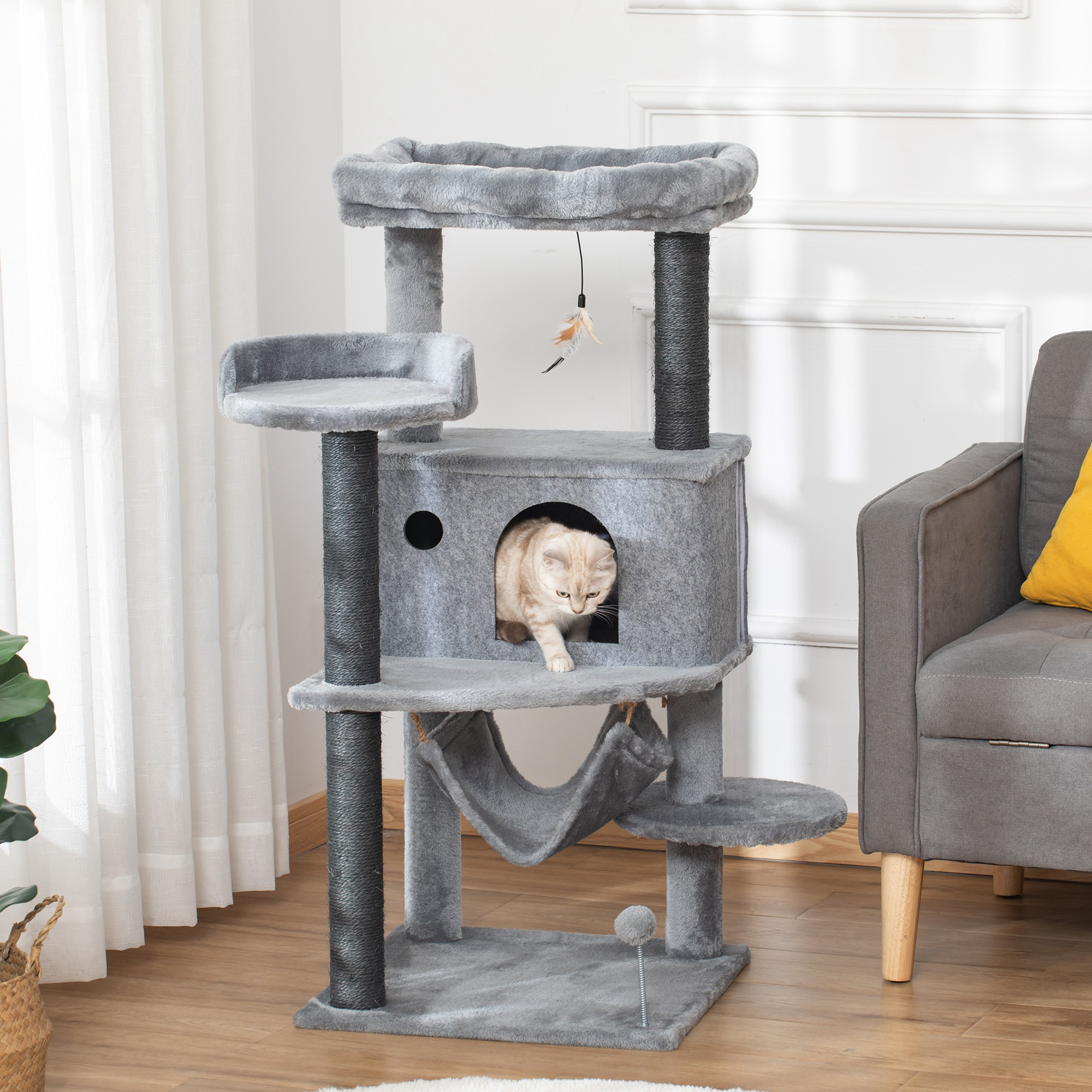 Un gatto chiaro esce da un tiragraffi grigio con amaca e giocattoli.