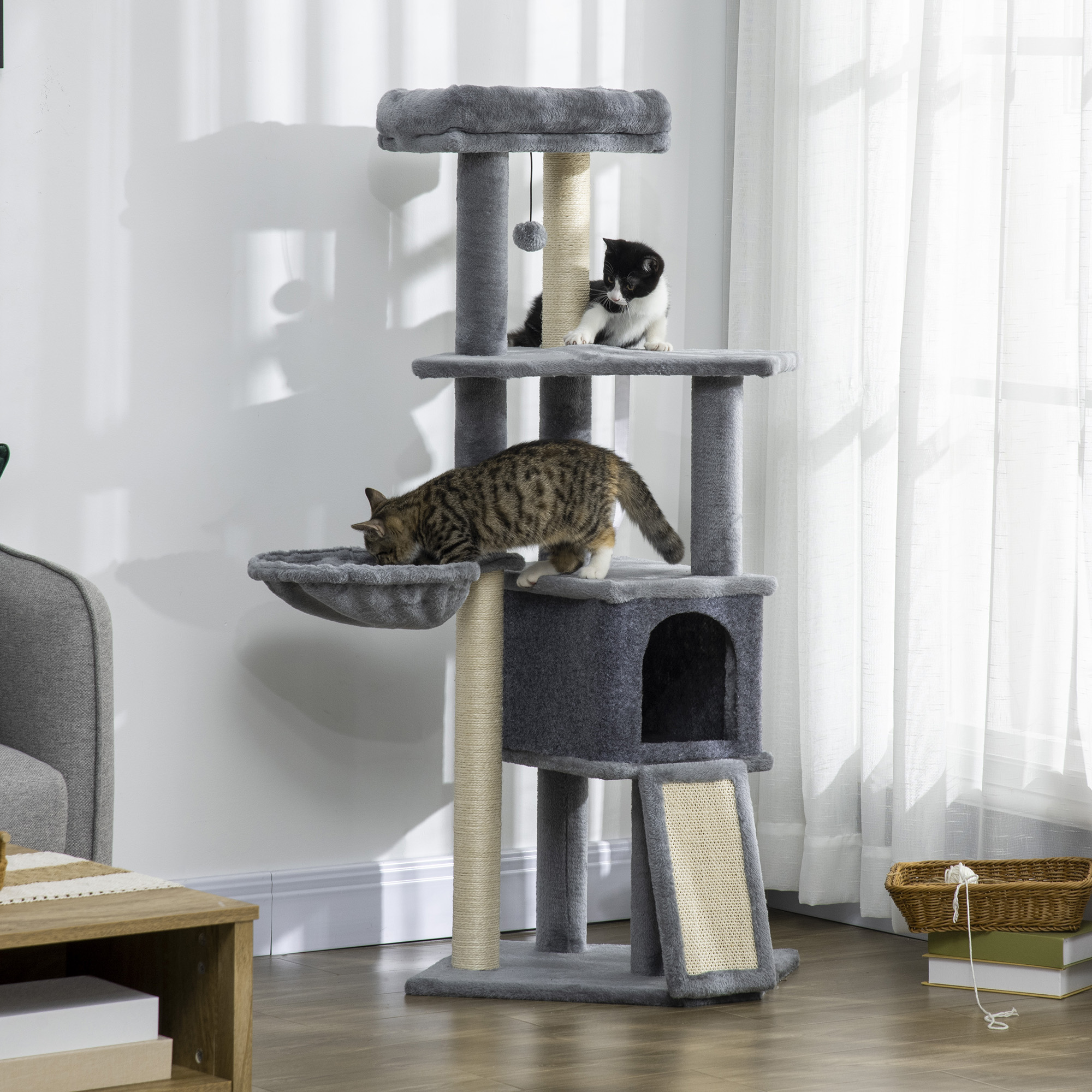 Dos gatos en un rascador gris con una cesta y libros al lado.