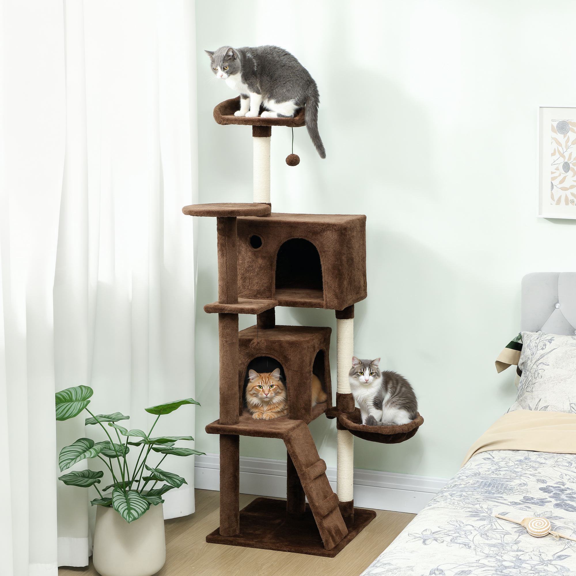 Tres gatos en un árbol rascador marrón con juguetes y plantas.