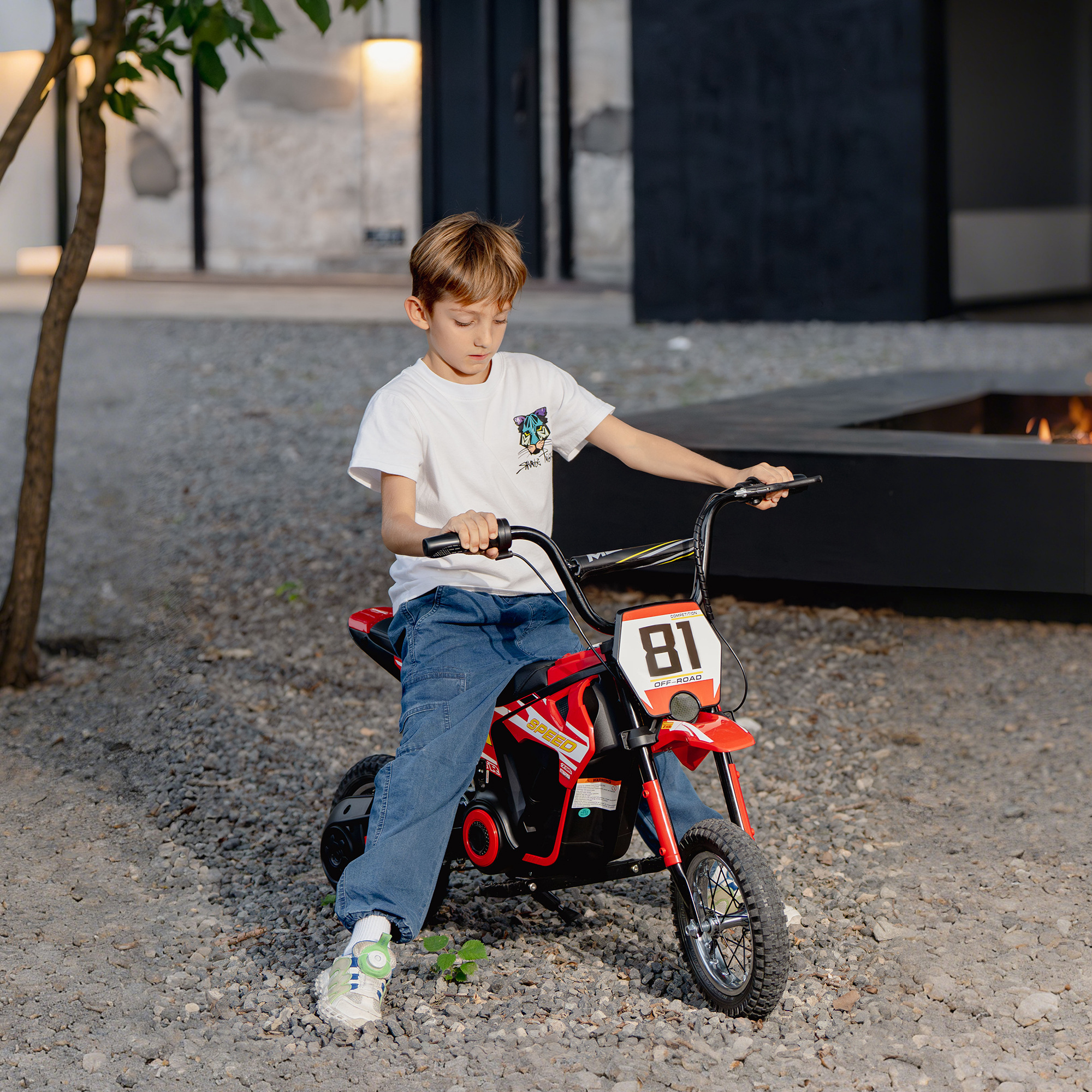 Un niño se sienta en una moto de juguete roja con el número 81.