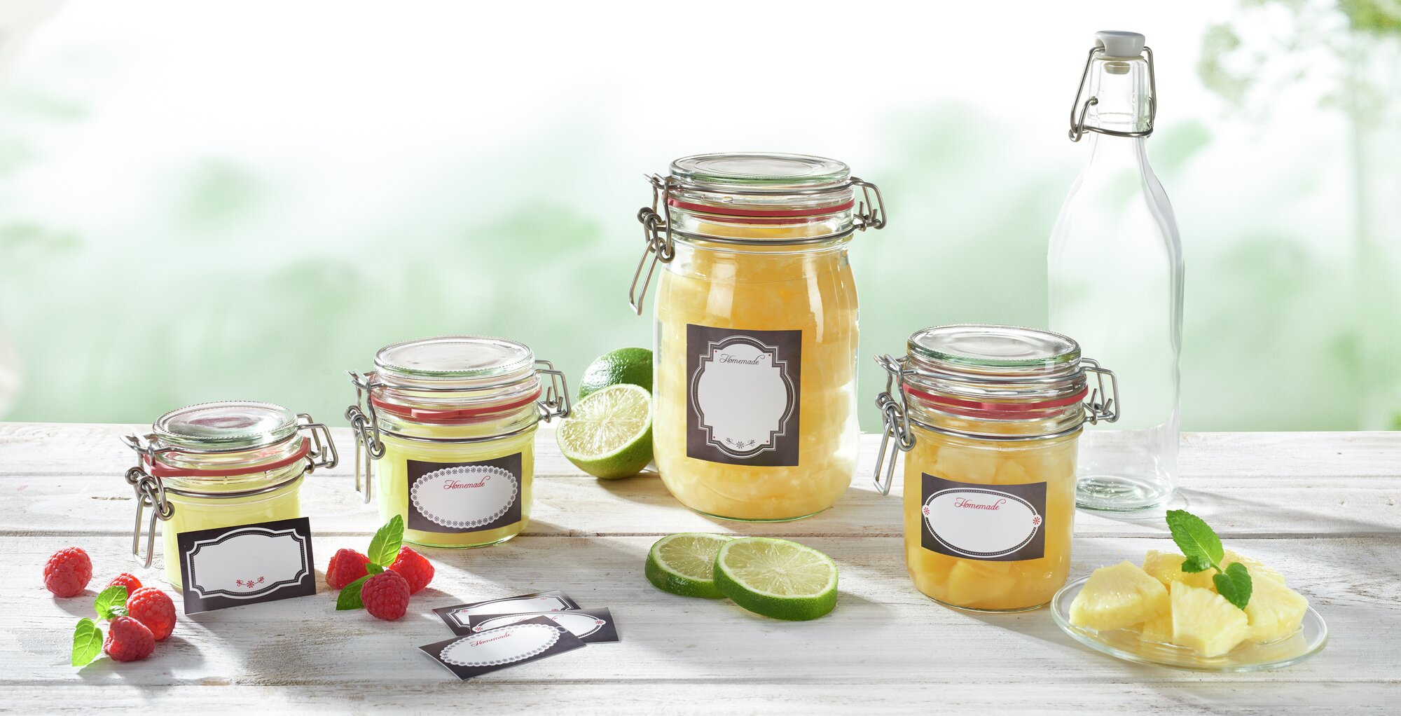 Vier Gläser mit hausgemachten Marmeladen, Beeren, Limetten und Ananas auf einem Holztisch.
