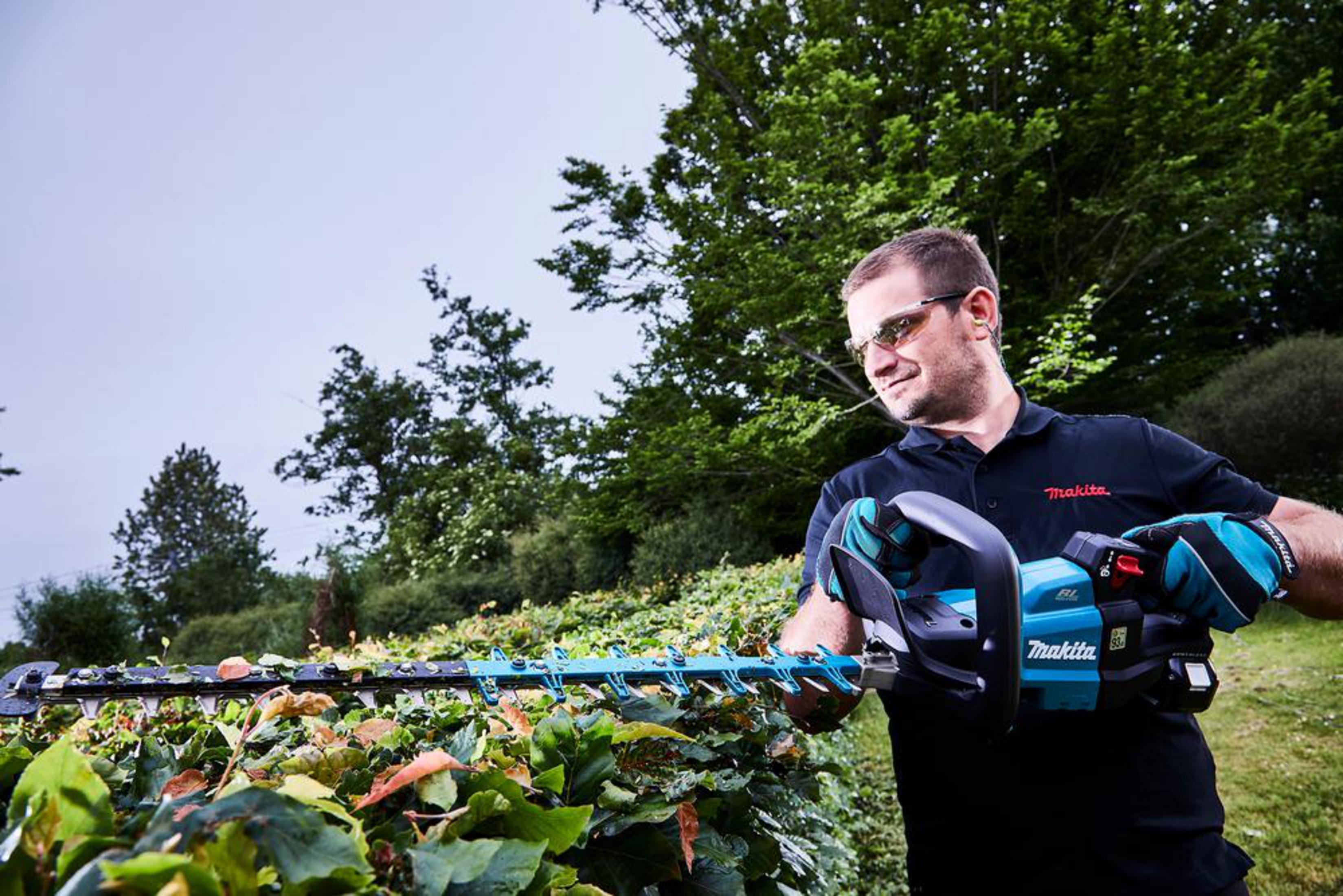 Mężczyzna z nożycami do żywopłotu przycina zielony krzew na zewnątrz.