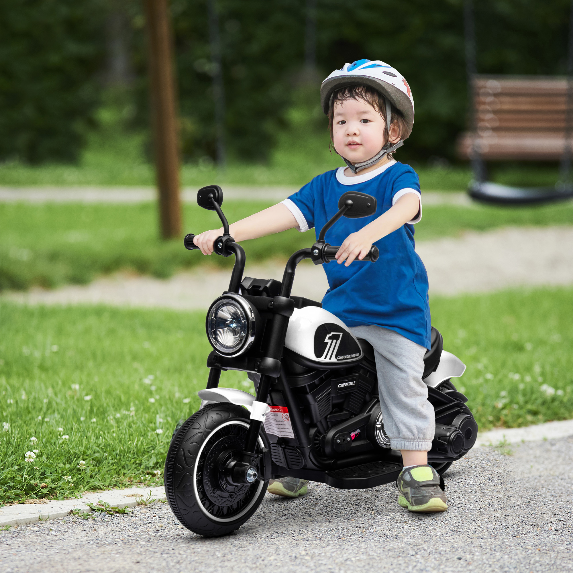 Un niño con casco monta una motocicleta de juguete blanca al aire libre en un camino de grava.