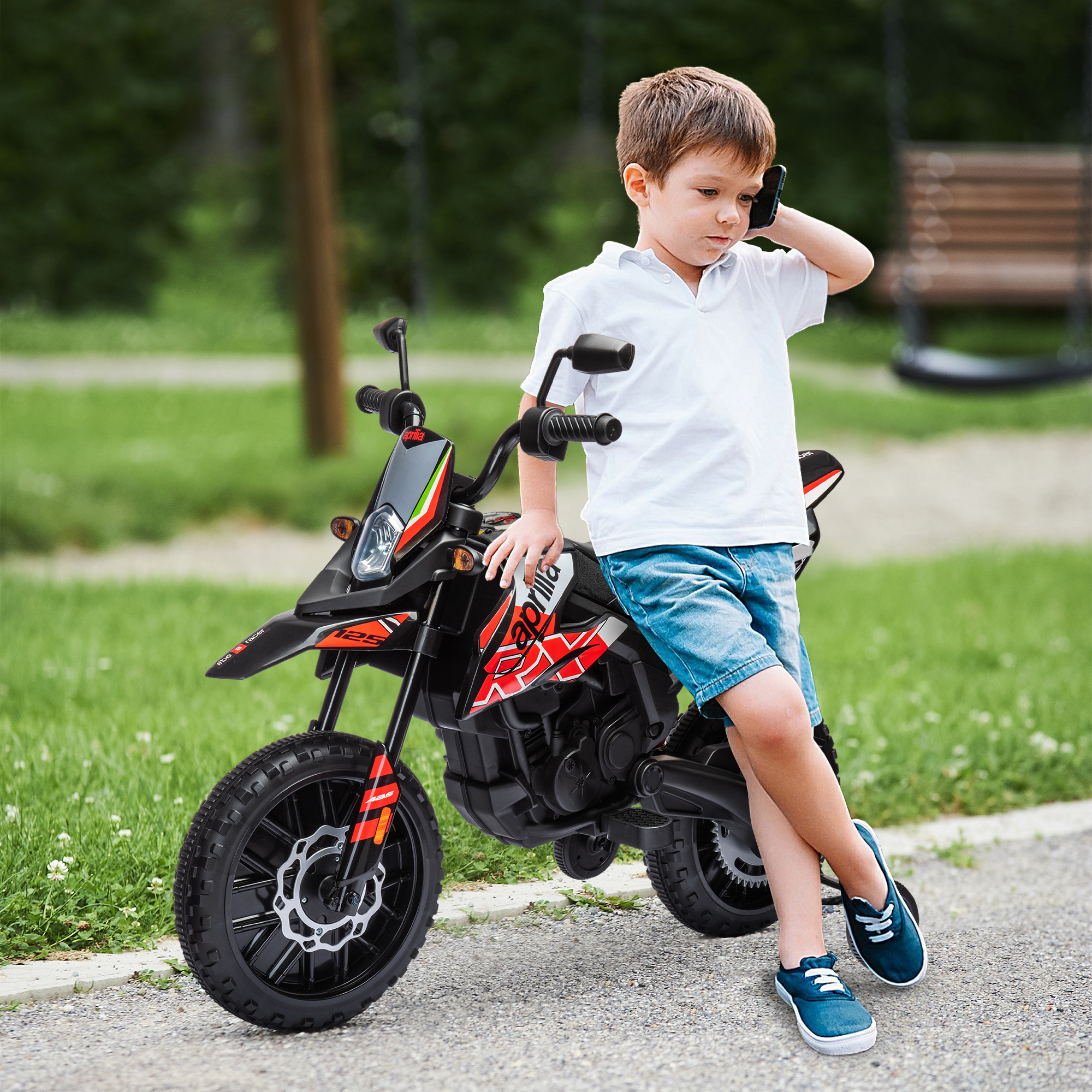 Un niño habla por celular, apoyado en una motocicleta de juguete al aire libre.