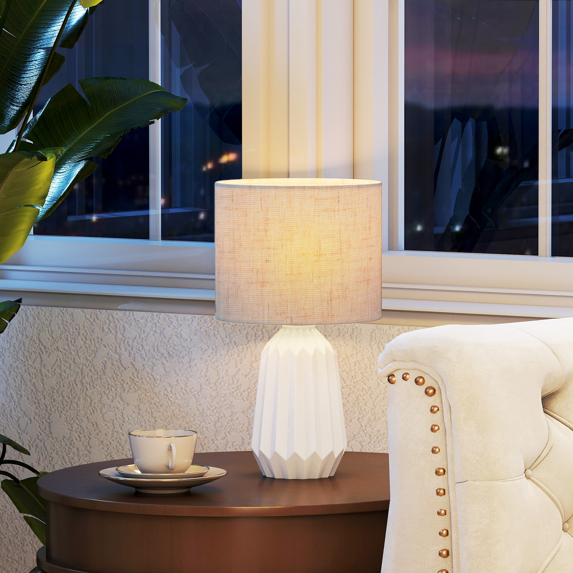 Una lámpara, una taza y un sillón junto a una ventana de noche.