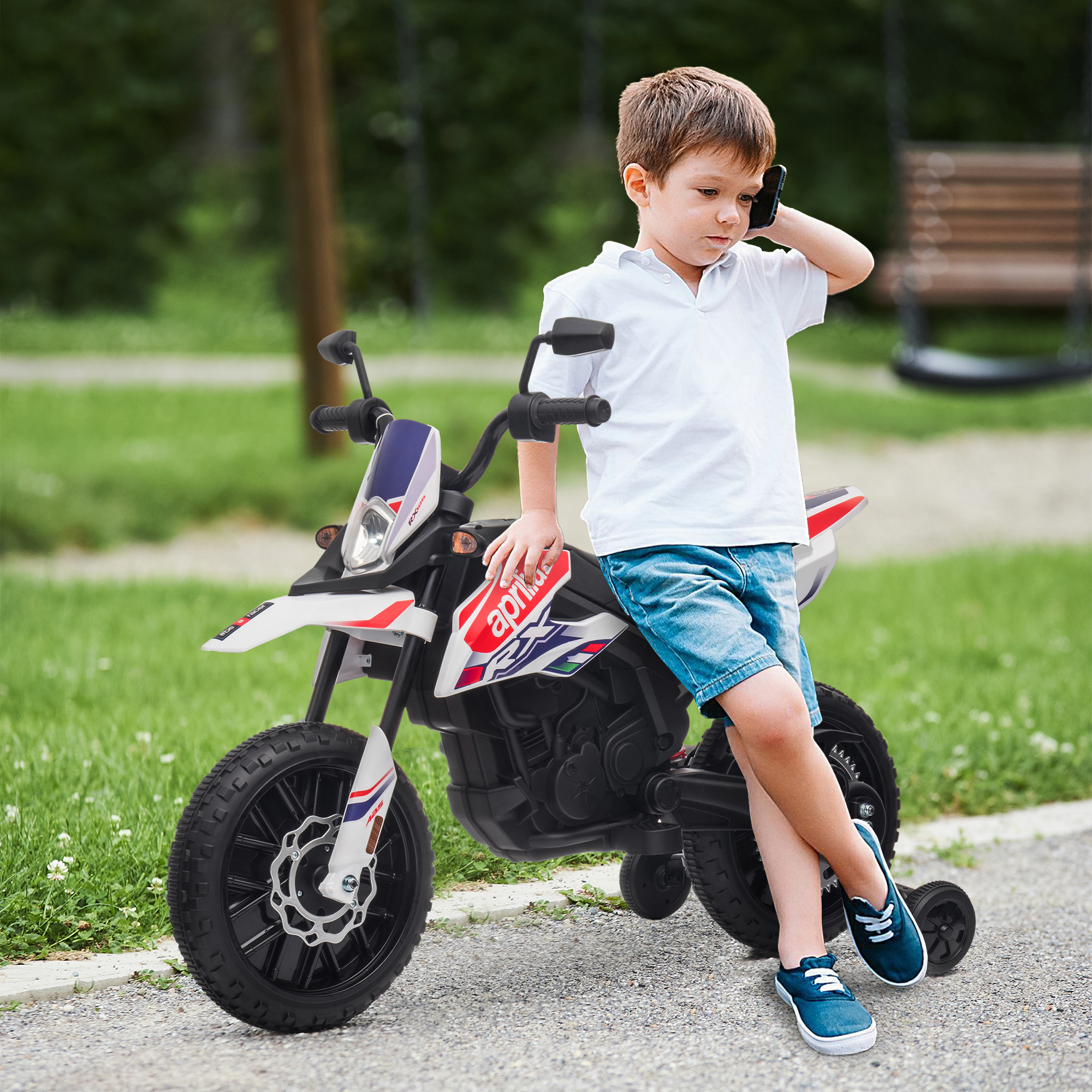 Un niño con polo blanco y shorts vaqueros se sienta en una moto de juguete, hablando por teléfono.