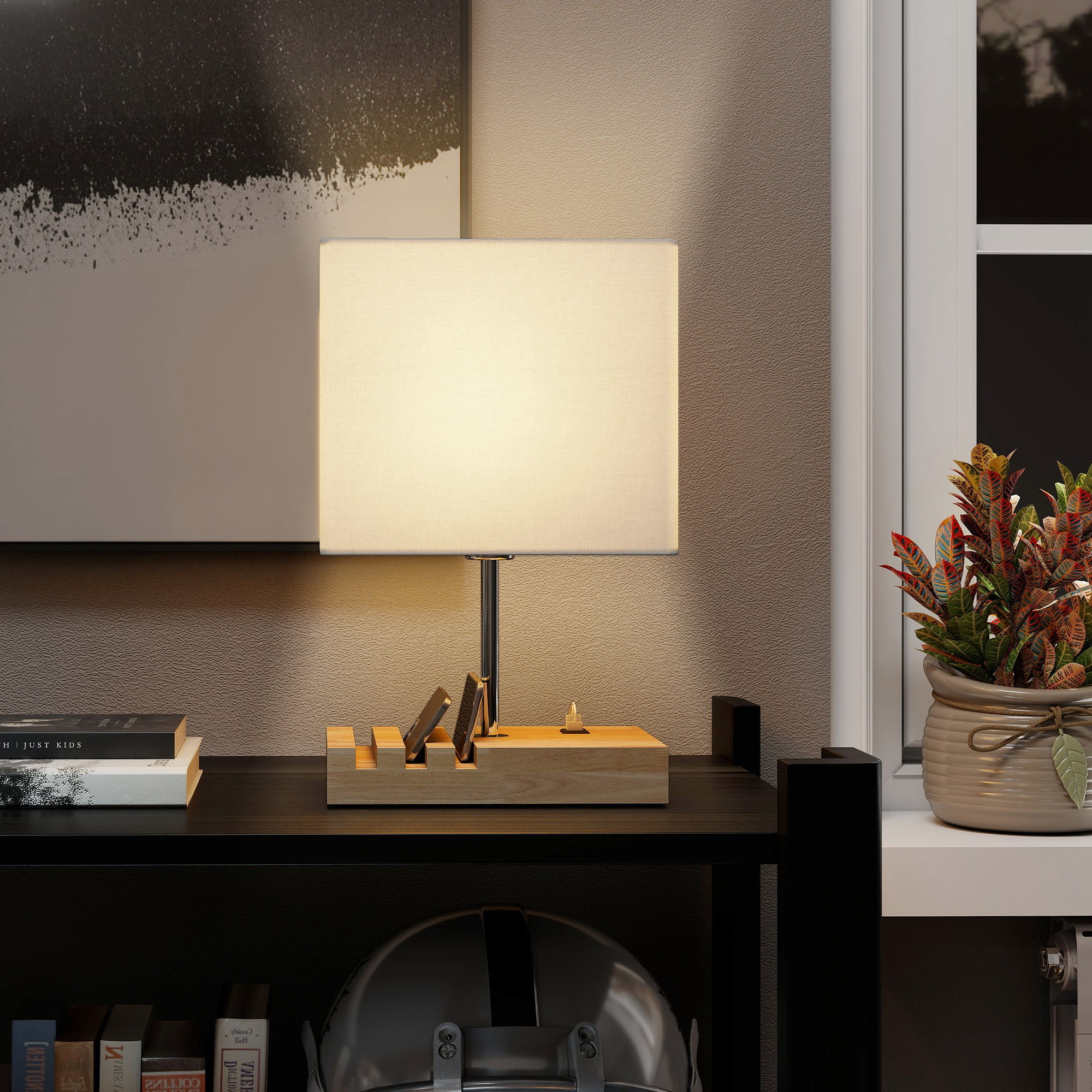 Una mesita de noche con lámpara, soporte para teléfono, libros y una planta junto a la ventana.