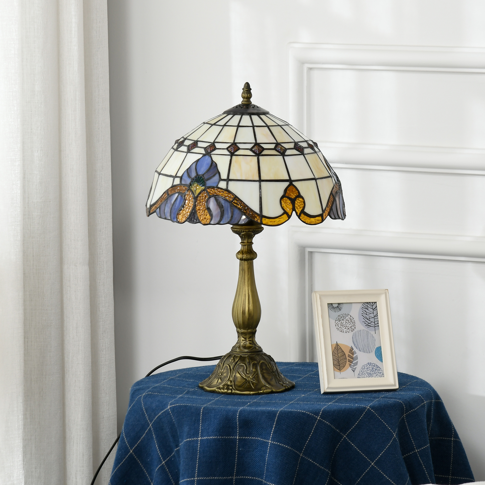 Lámpara de mesa Tiffany de vidrieras con patrón floral azul sobre mantel azul a cuadros.