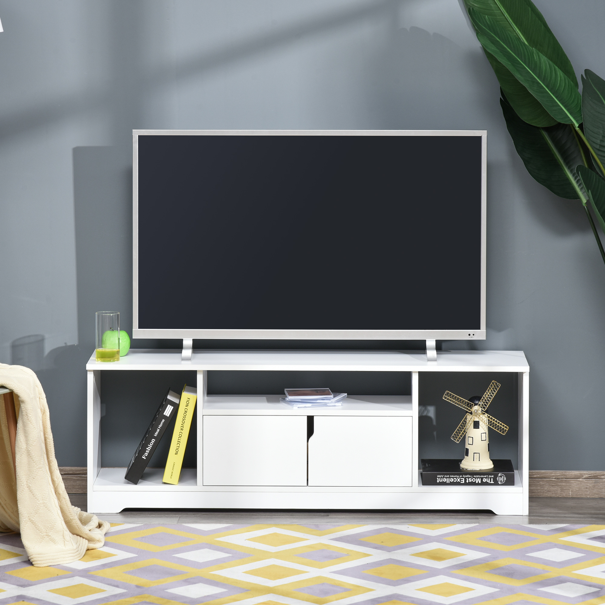 Un mueble de TV blanco con TV, libros, una lámpara y decoración de molino.