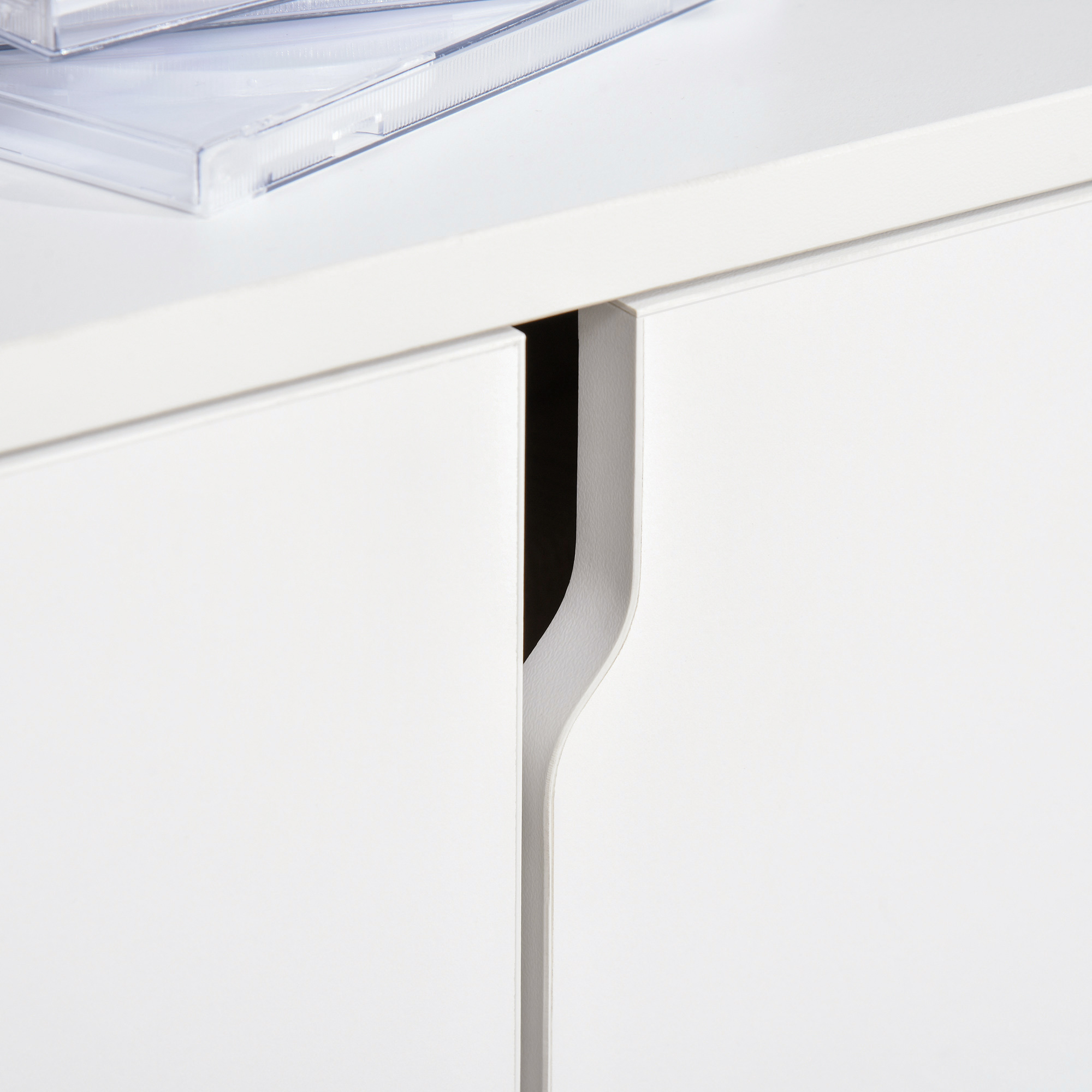 Frentes de cajón blancos con un tirador empotrado, estuches de CD encima.