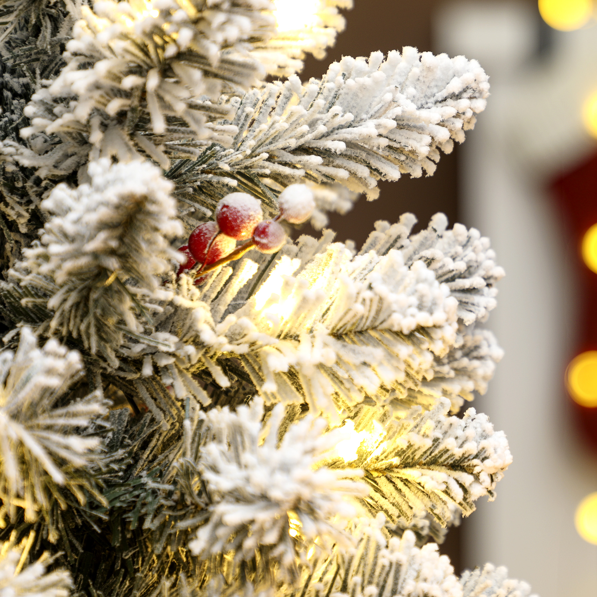 Primer plano de un árbol de Navidad con nieve, bayas rojas y luces.