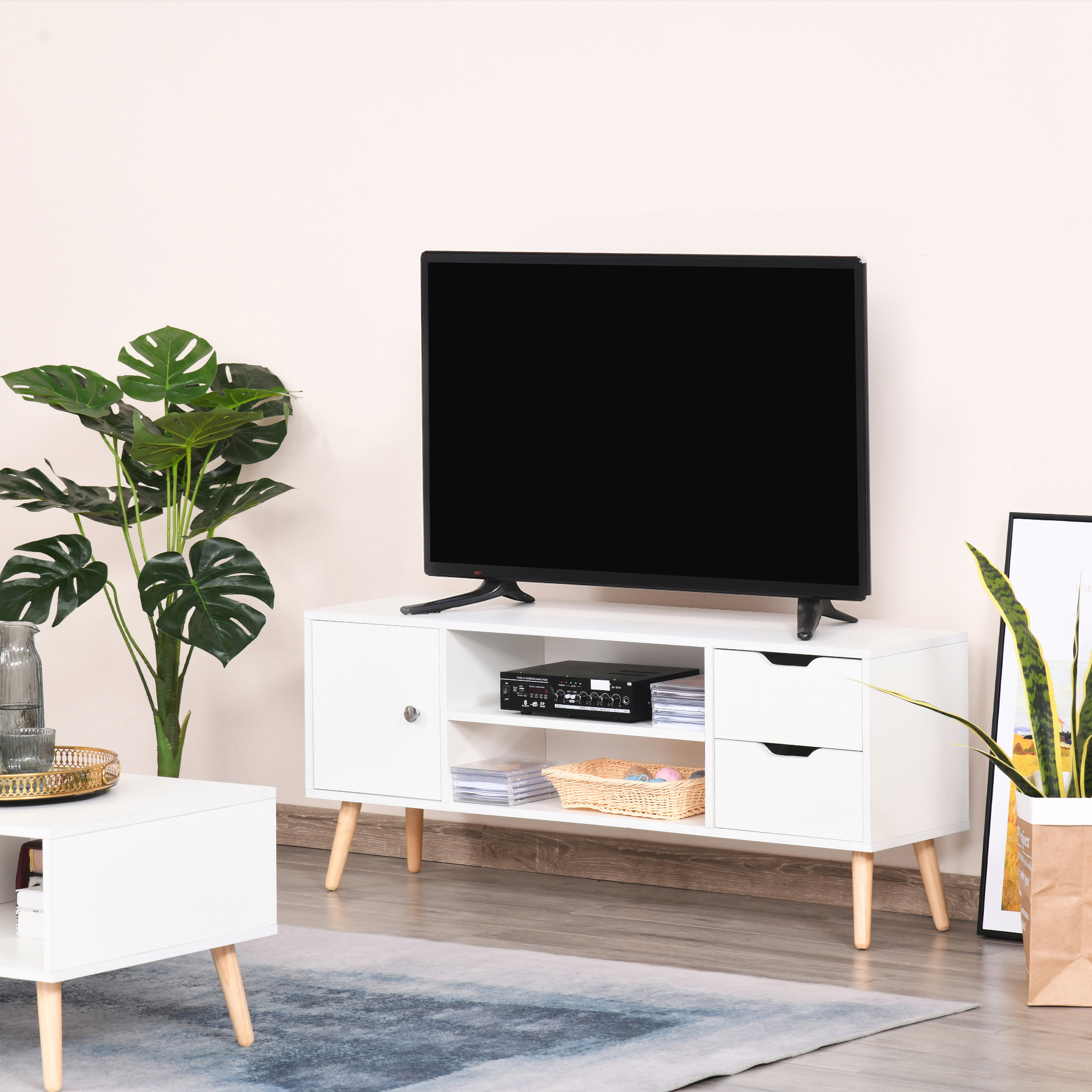 Un mueble de TV blanco moderno con TV de pantalla plana, plantas y arte.