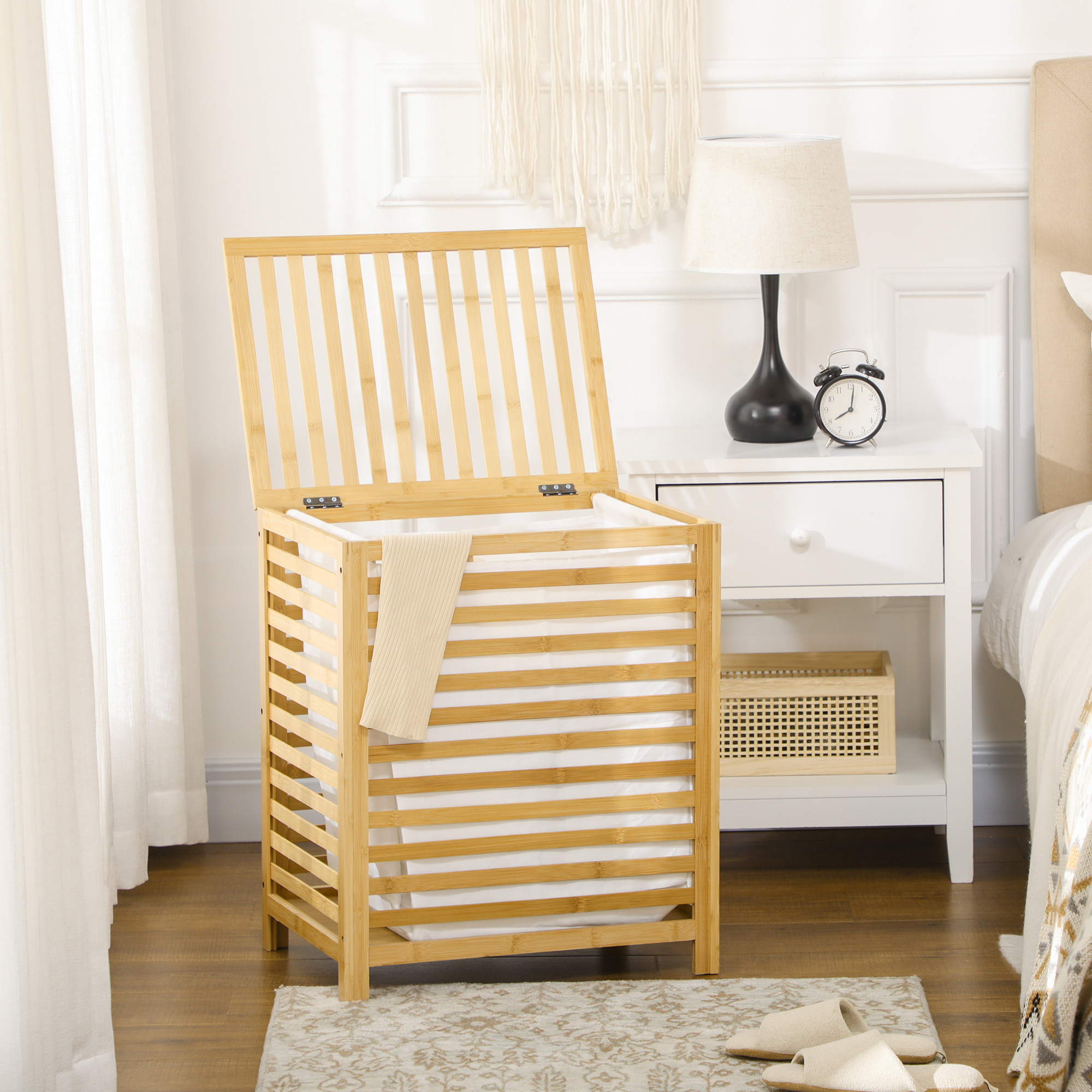 Un cesto de ropa de madera con tapa junto a una mesita de noche con lámpara y despertador.