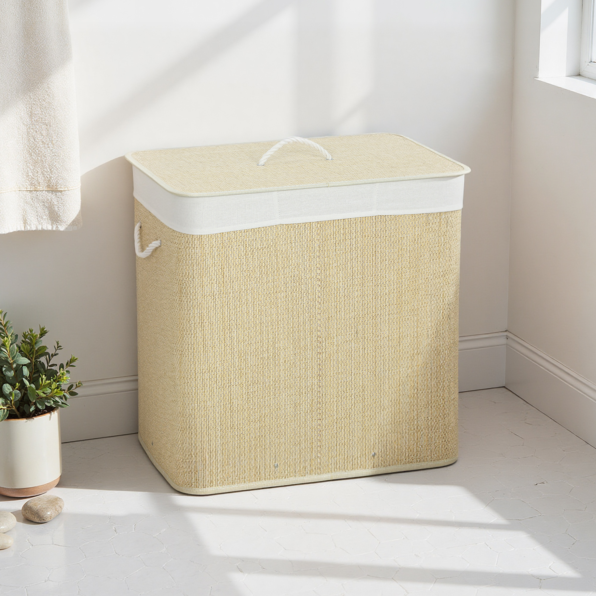 Una cesta de lavandería beige con tapa blanca y asa de cuerda está en un suelo claro.
