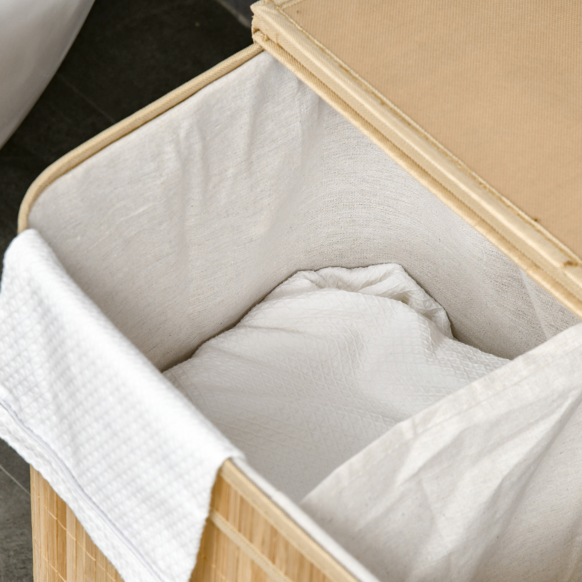 Una cesta de lavandería de bambú abierta forrada de tela blanca, con ropa blanca.