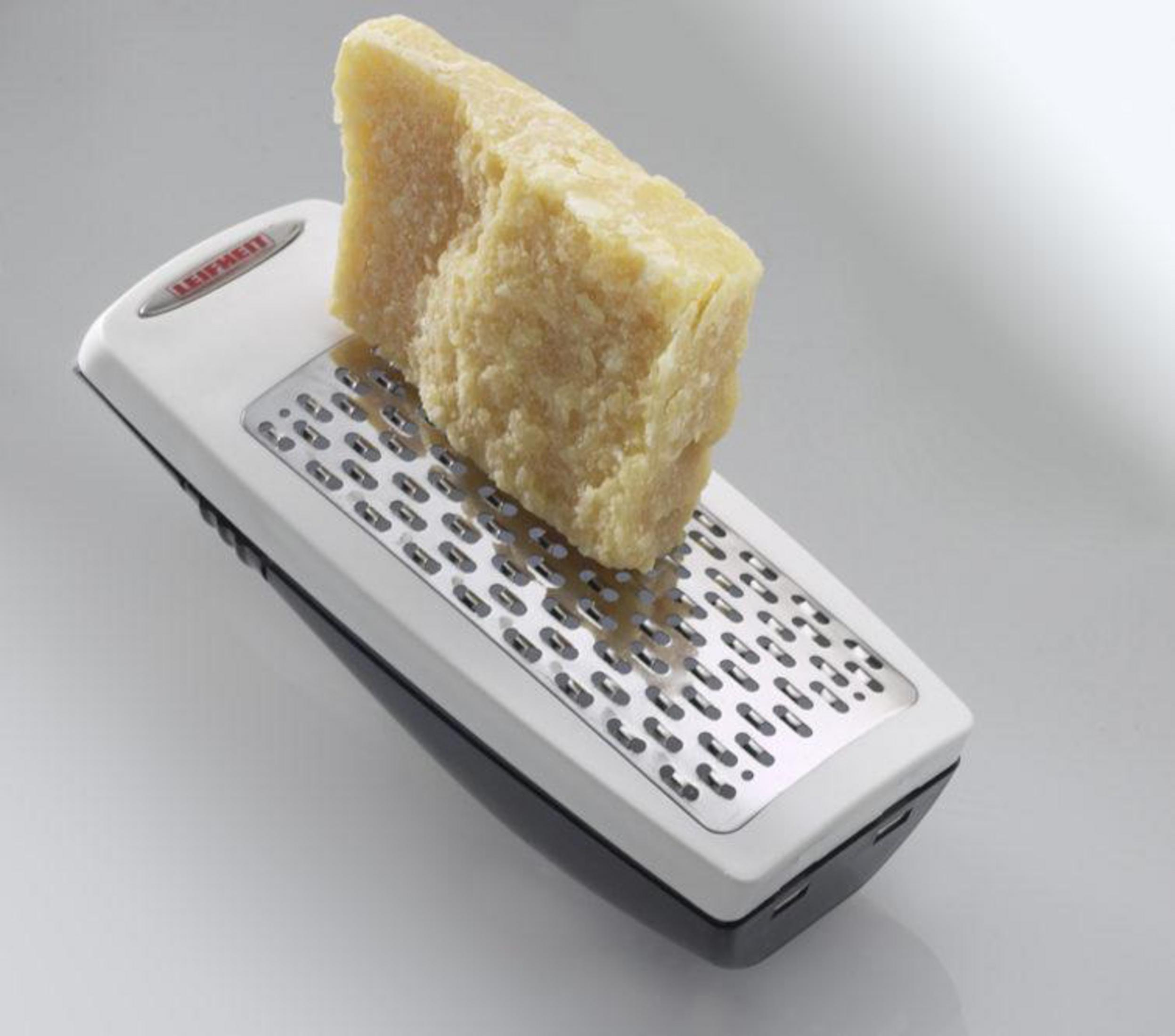 Ein Block Parmesan liegt auf einem weißen Käsereibe mit schwarzem Griff.
