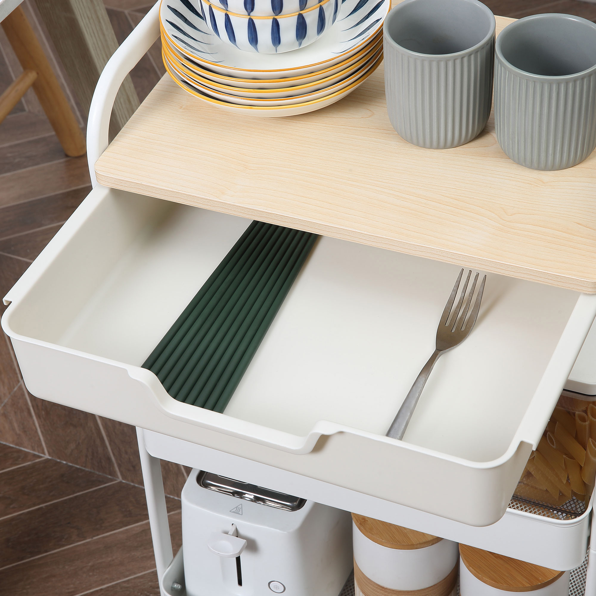 Un carrito auxiliar blanco con platos, tazas y un cajón con cubiertos.