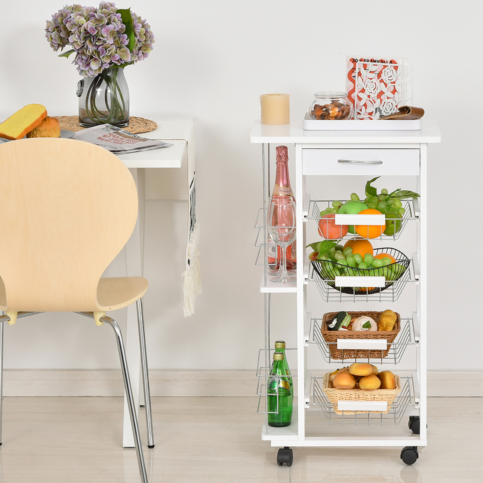 Un carrito auxiliar blanco con fruta, pan y bebidas junto a una mesa.