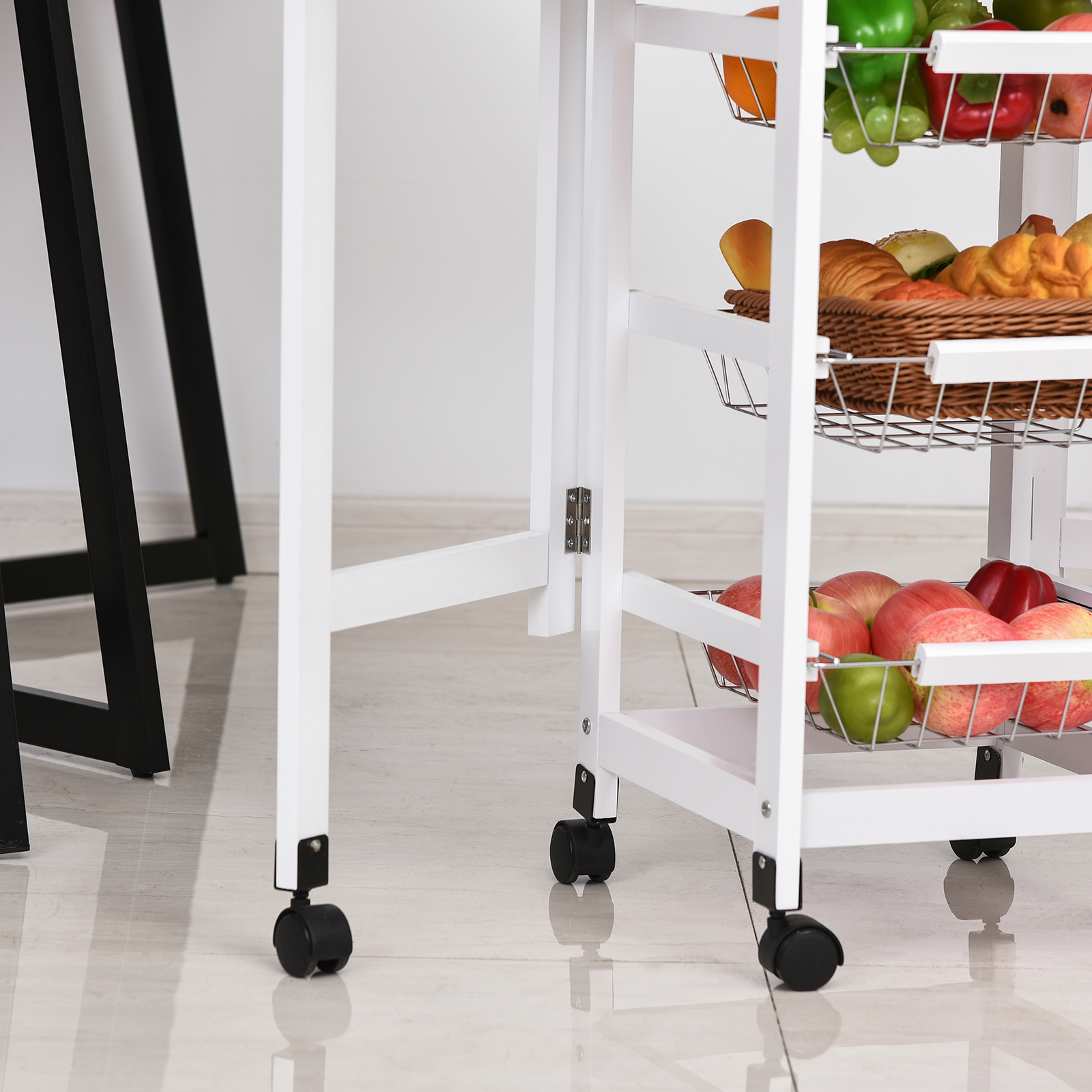Un carrito blanco con ruedas, con frutas y pan. Patas de mesa negras al fondo.