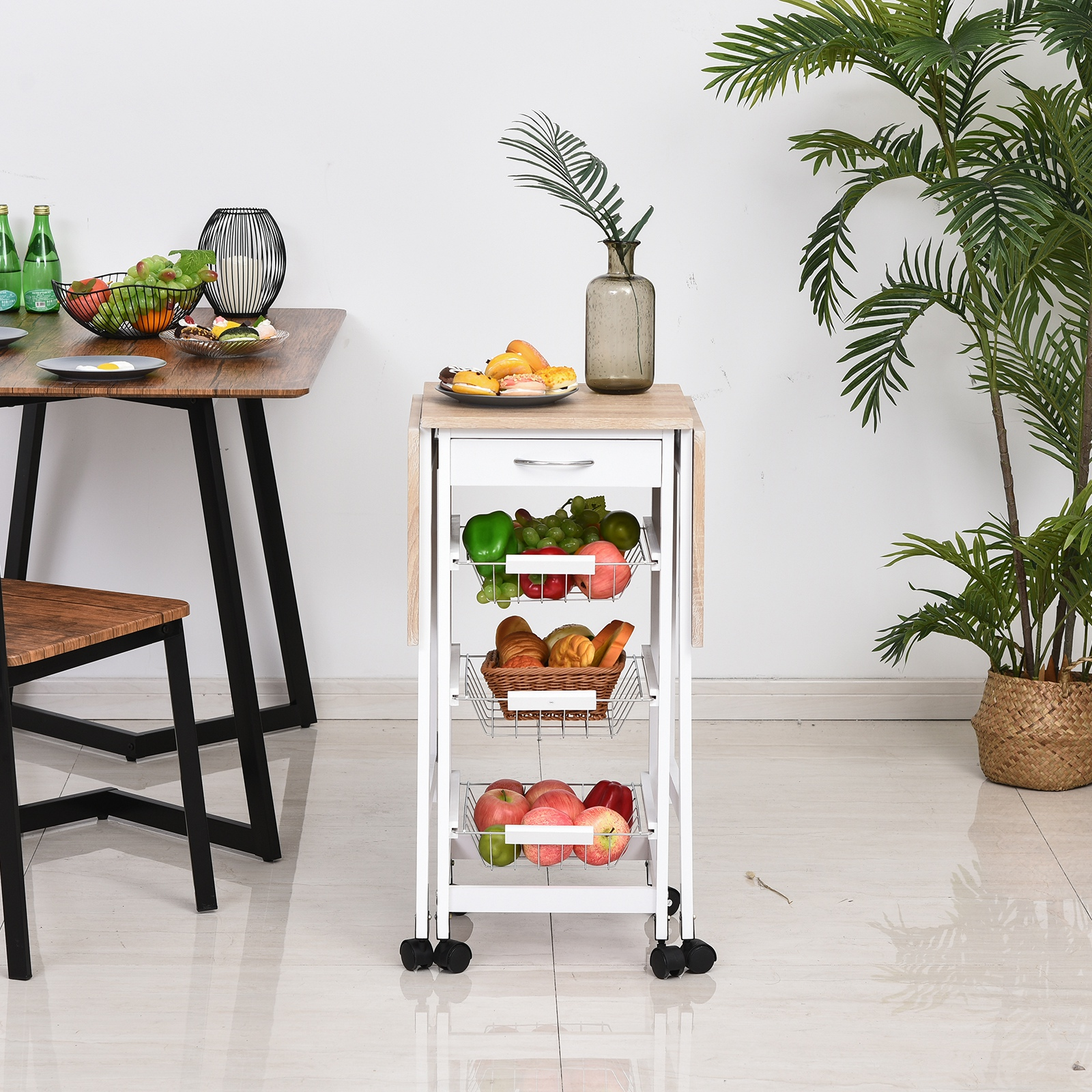Un carrito auxiliar blanco con tres cestas de fruta y pan está junto a una mesa de madera.