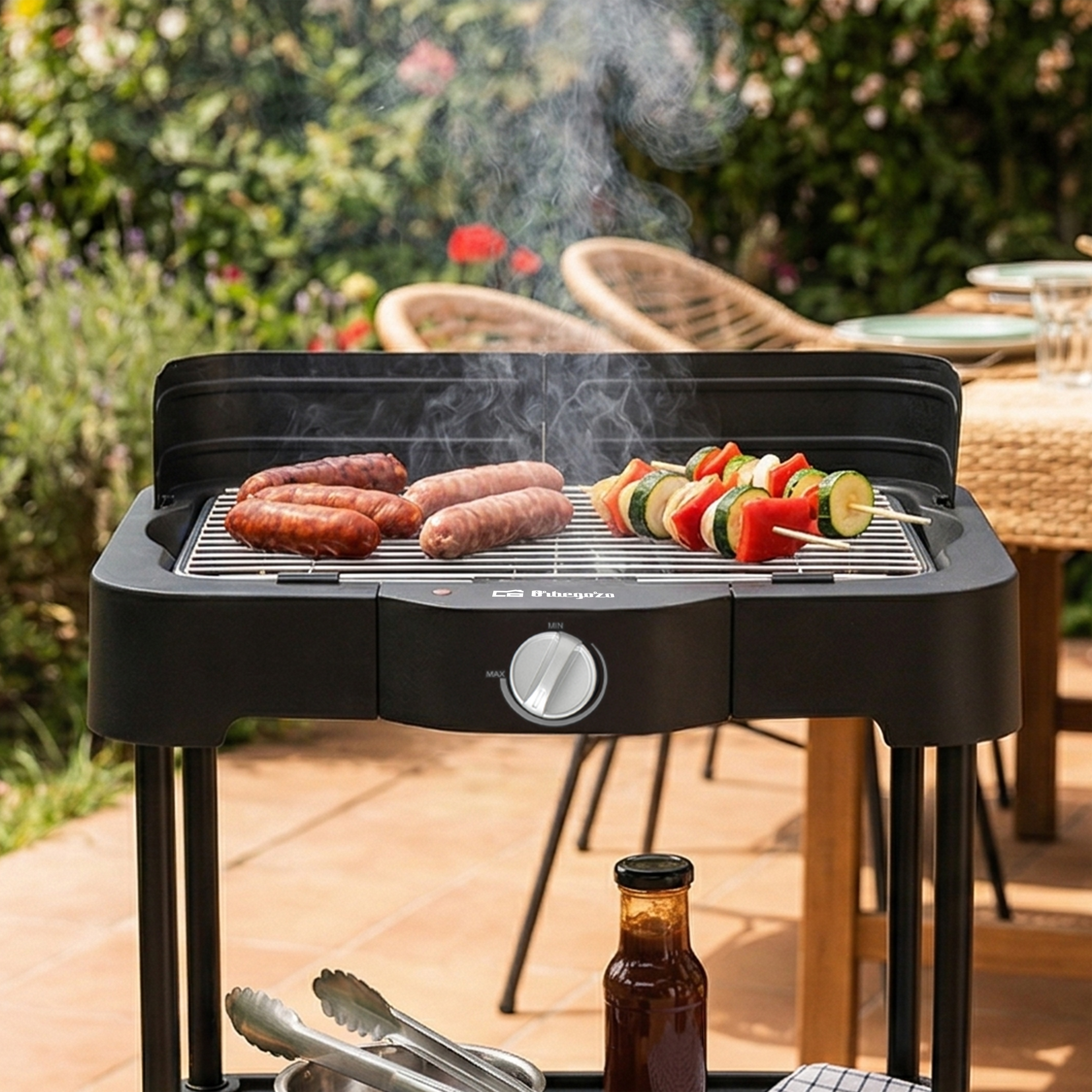 Una parrilla eléctrica con salchichas y brochetas de verduras en un jardín.