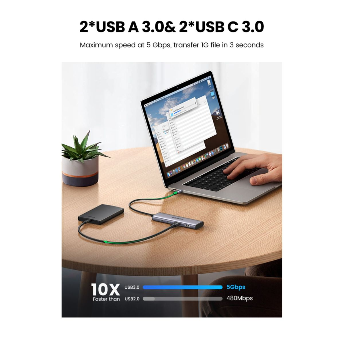 Laptop podłączony do huba, dysku zewnętrznego i rośliny doniczkowej na stole.