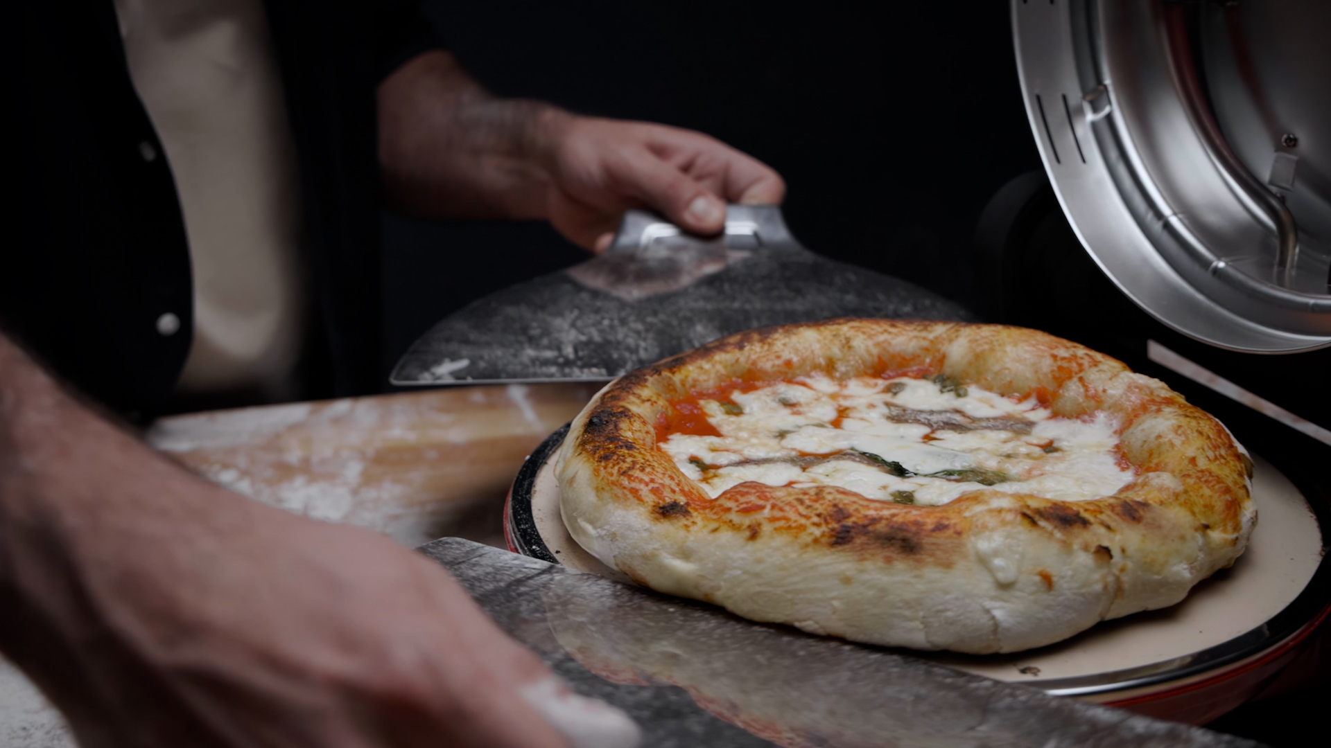 Eine Person benutzt einen Pizzaschieber, um eine frisch gebackene Pizza aus einem Ofen zu nehmen.