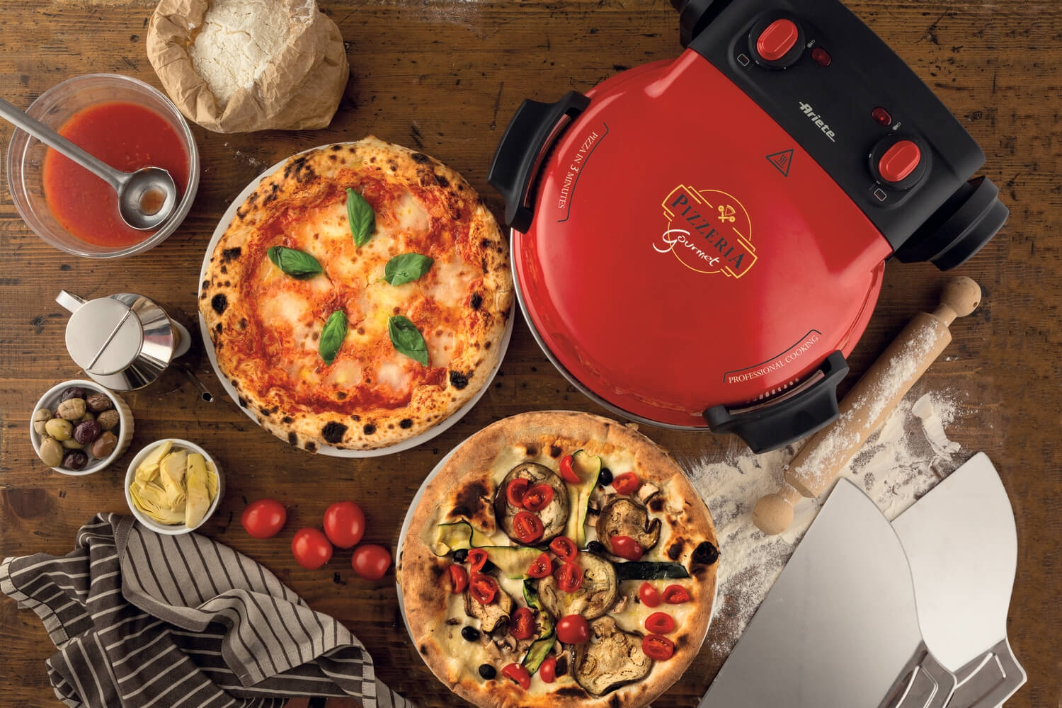 Roter Pizzaofen mit zwei Pizzen, Tomatensoße, Oliven, Artischocken und Pizzaschaufeln.