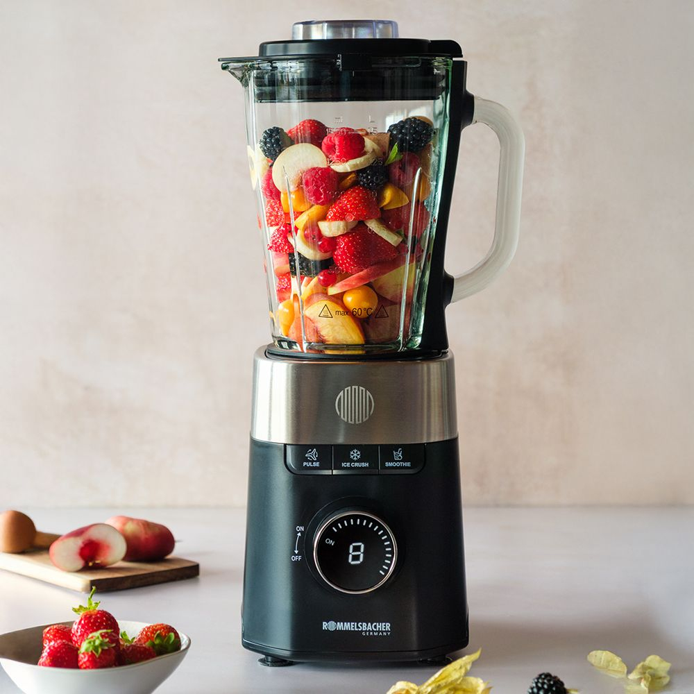 Ein Mixer mit Glasbehälter, gefüllt mit Früchten wie Erdbeeren, Beeren und Pfirsichen.