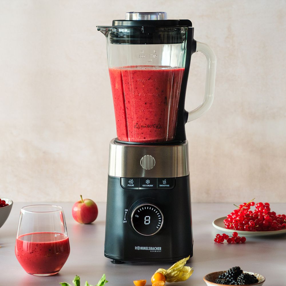 Ein schwarzer Mixer mit rotem Smoothie, daneben Beeren und ein Apfel.