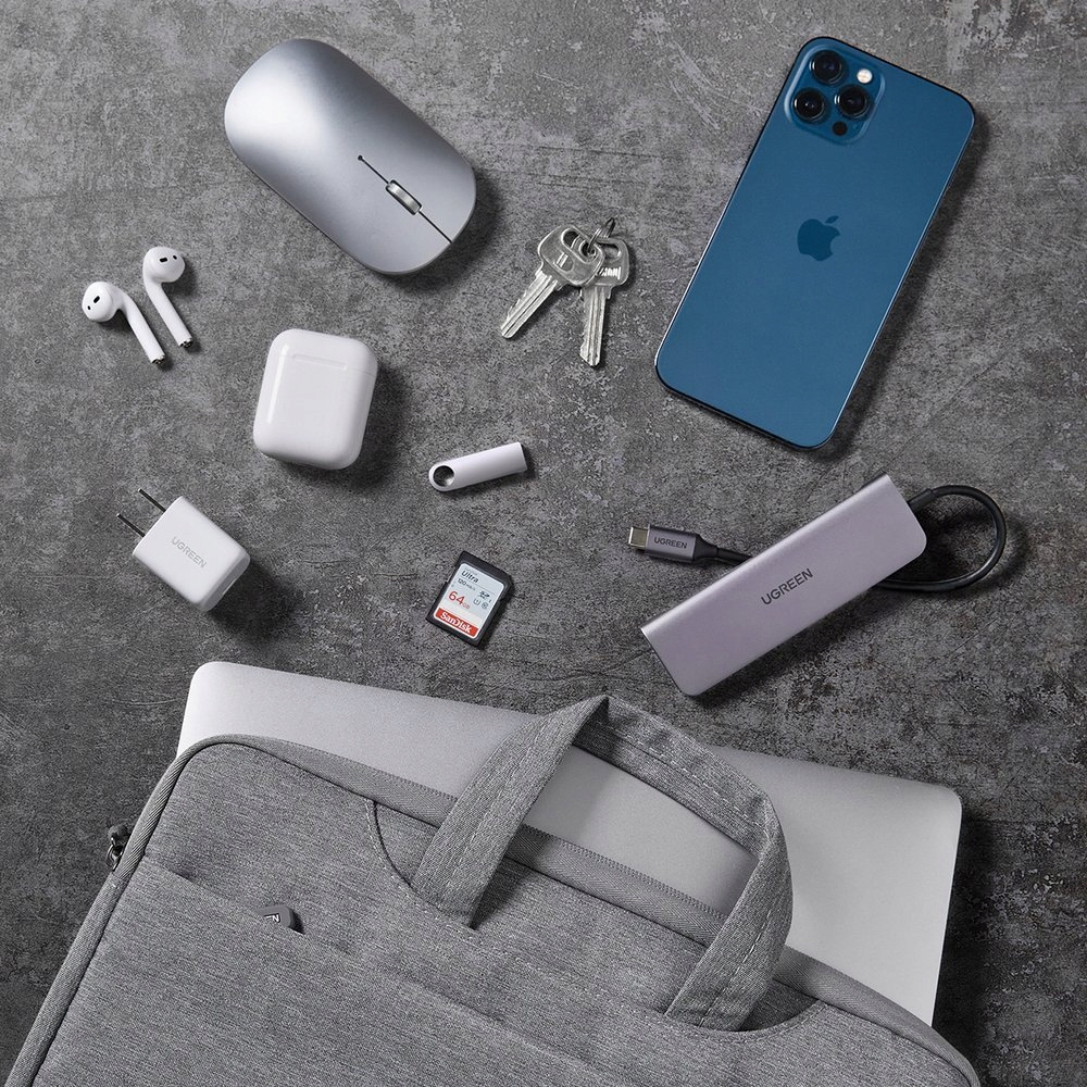 Niebieski iPhone, srebrna mysz, klucze, słuchawki, ładowarka, karta SD i hub na ciemnej powierzchni.