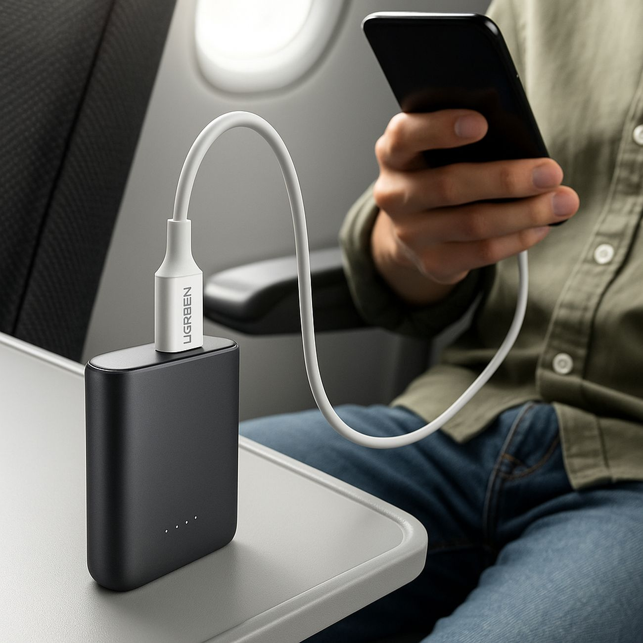 Czarny power bank ładuje smartfona na stoliku w samolocie.