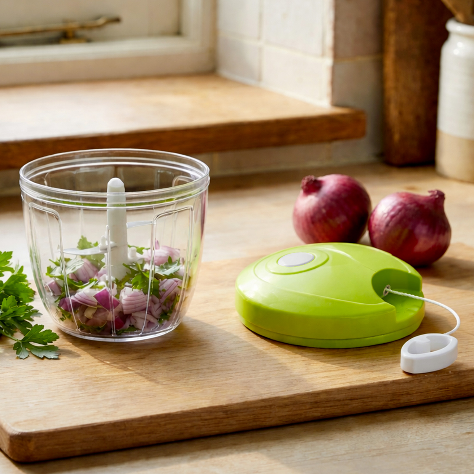 Un tritatutto manuale con cipolle e erbe tritate, accanto a due cipolle rosse.