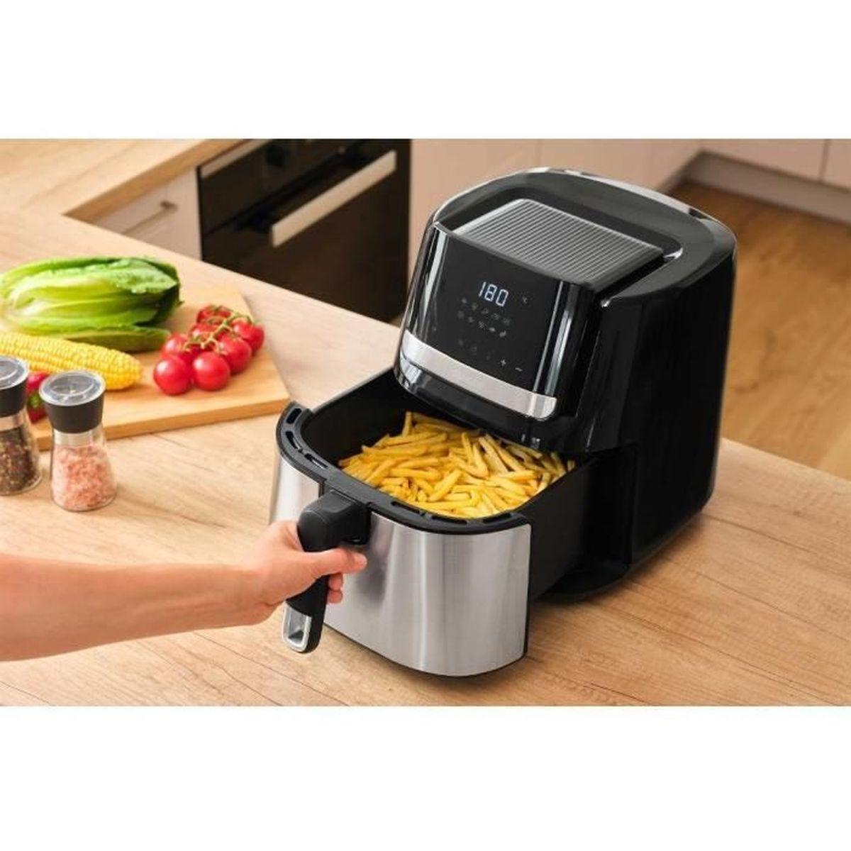 Una mano estrae il cassetto di una friggitrice ad aria nera piena di patatine fritte.
