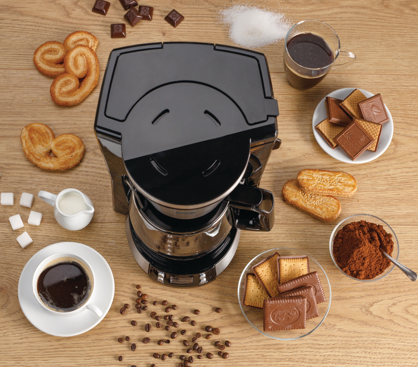 Kaffeemaschine mit Gebäck, Kaffee, Zucker und Schokostückchen auf Holztisch.