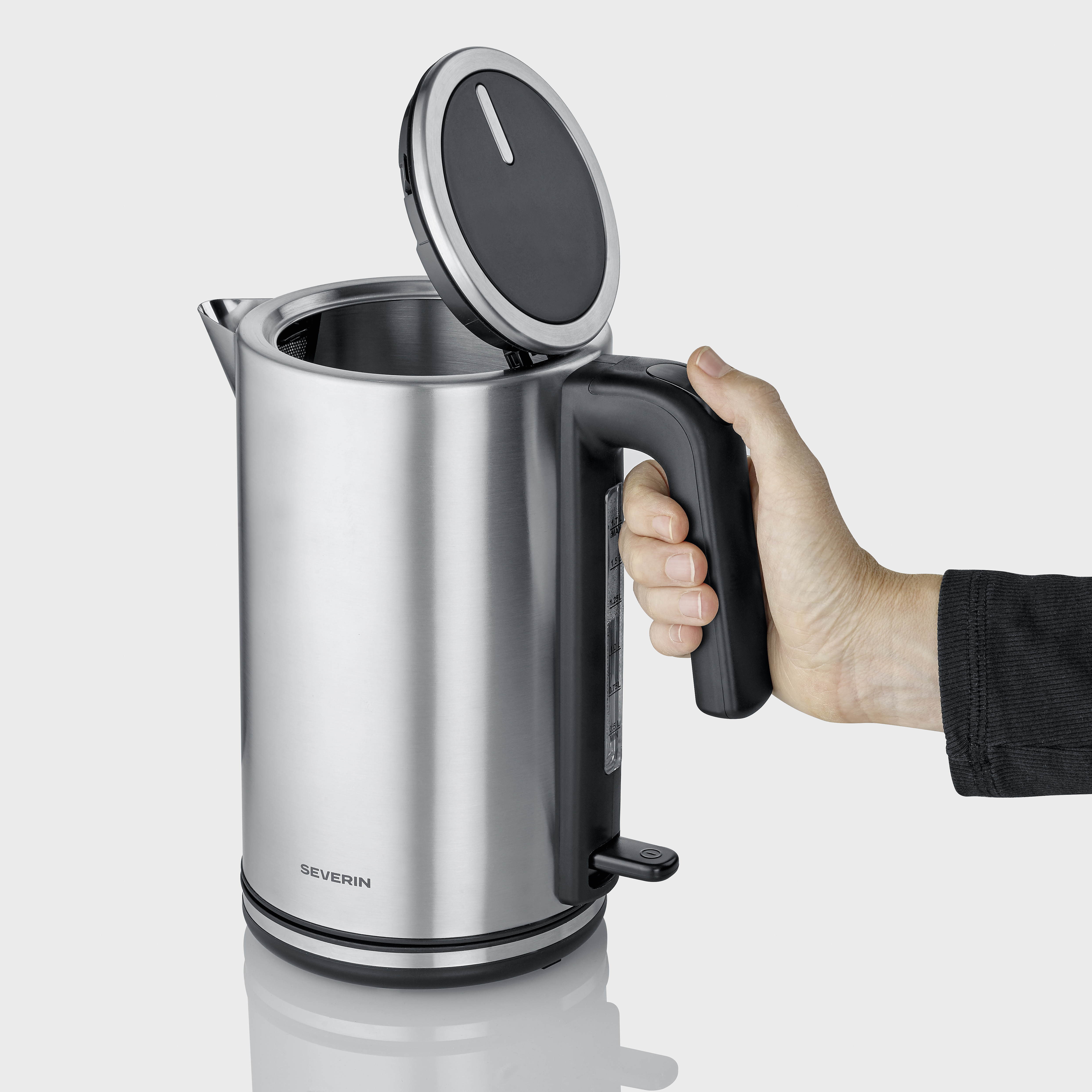 Una mano apre il coperchio di un bollitore argentato con manico nero.