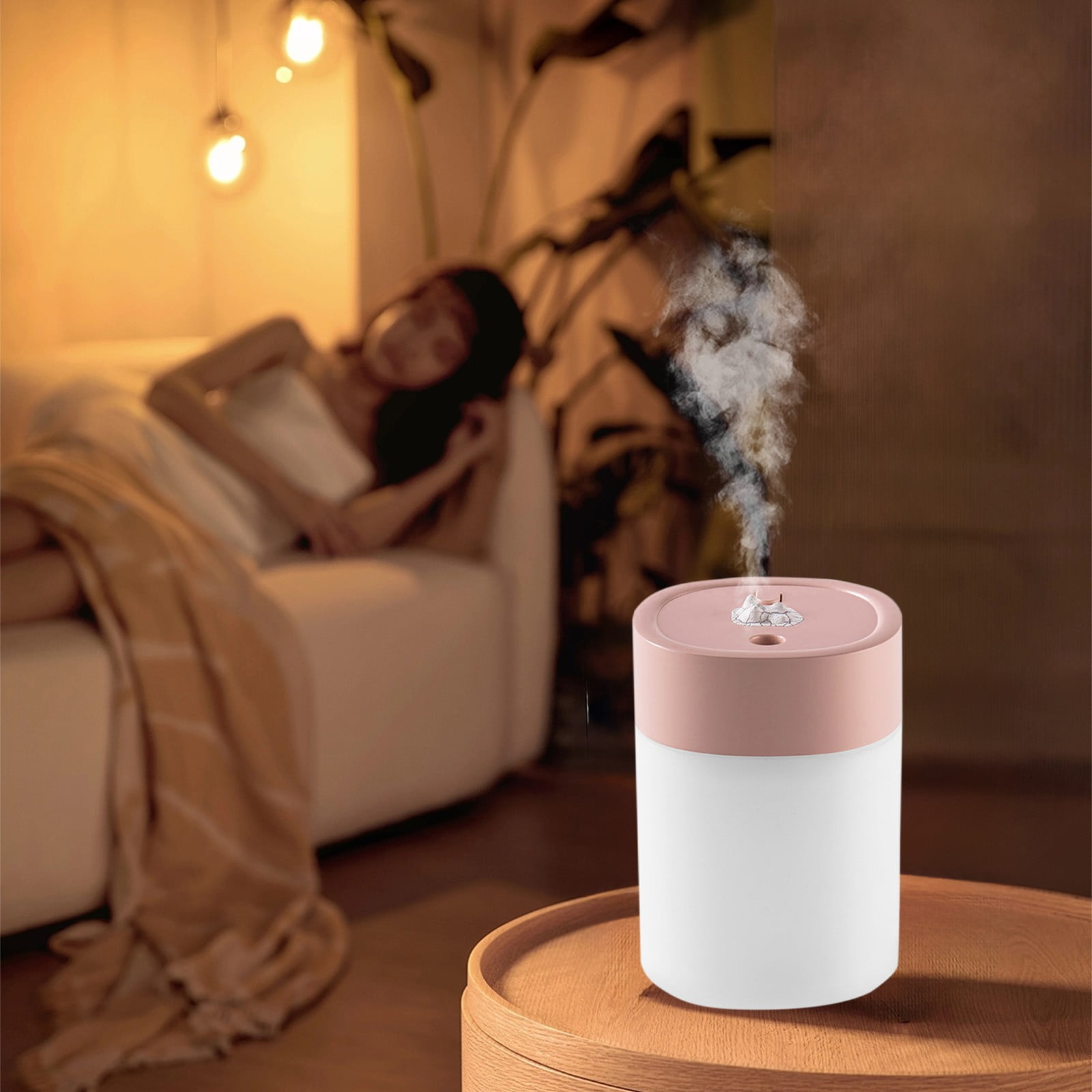 Ein rosa und weißer Luftbefeuchter mit Dampf auf einem Holztisch, im Hintergrund ruht eine Frau.