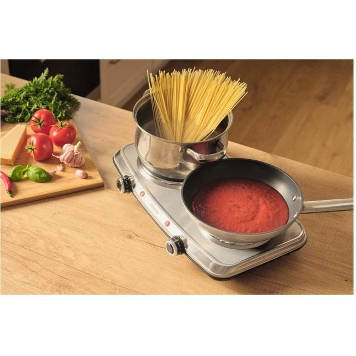 Spaghetti che cuociono in pentola, sugo in padella su doppio fornello.