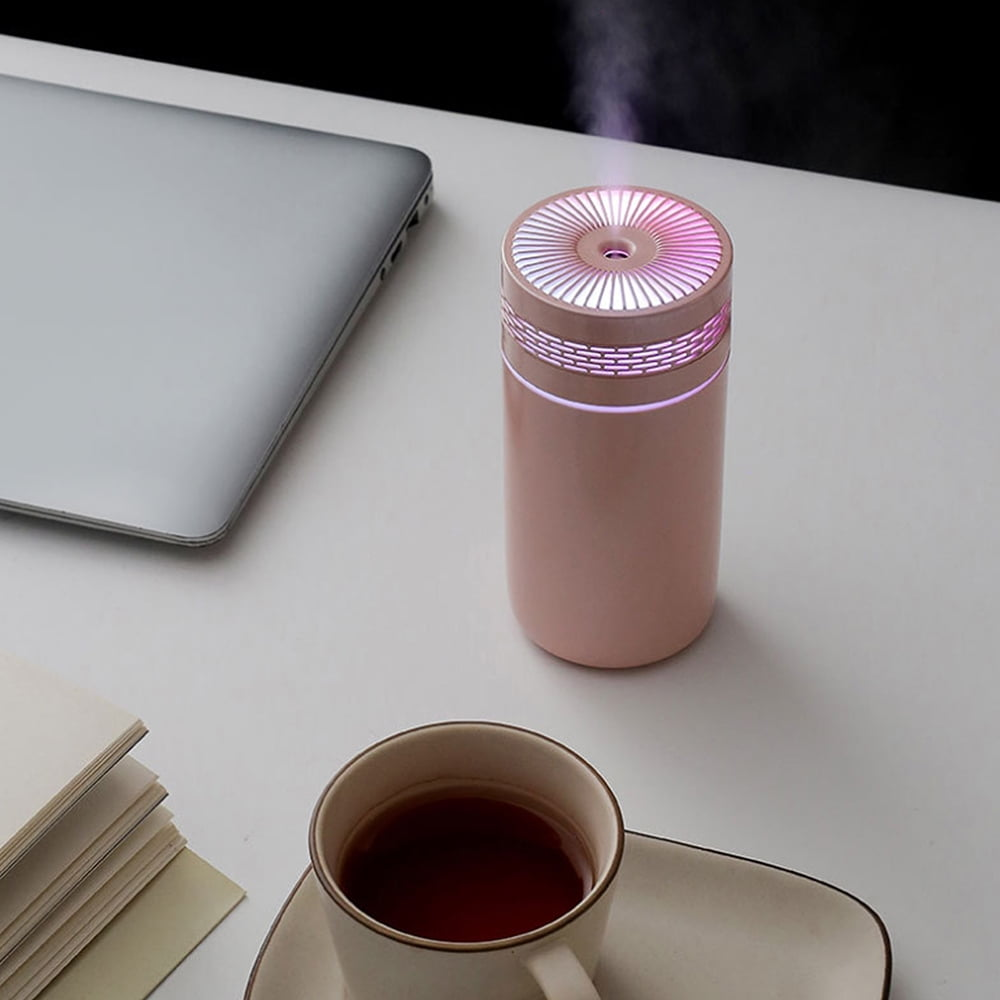 Ein rosa Luftbefeuchter mit Licht neben einem Laptop und einer Kaffeetasse.