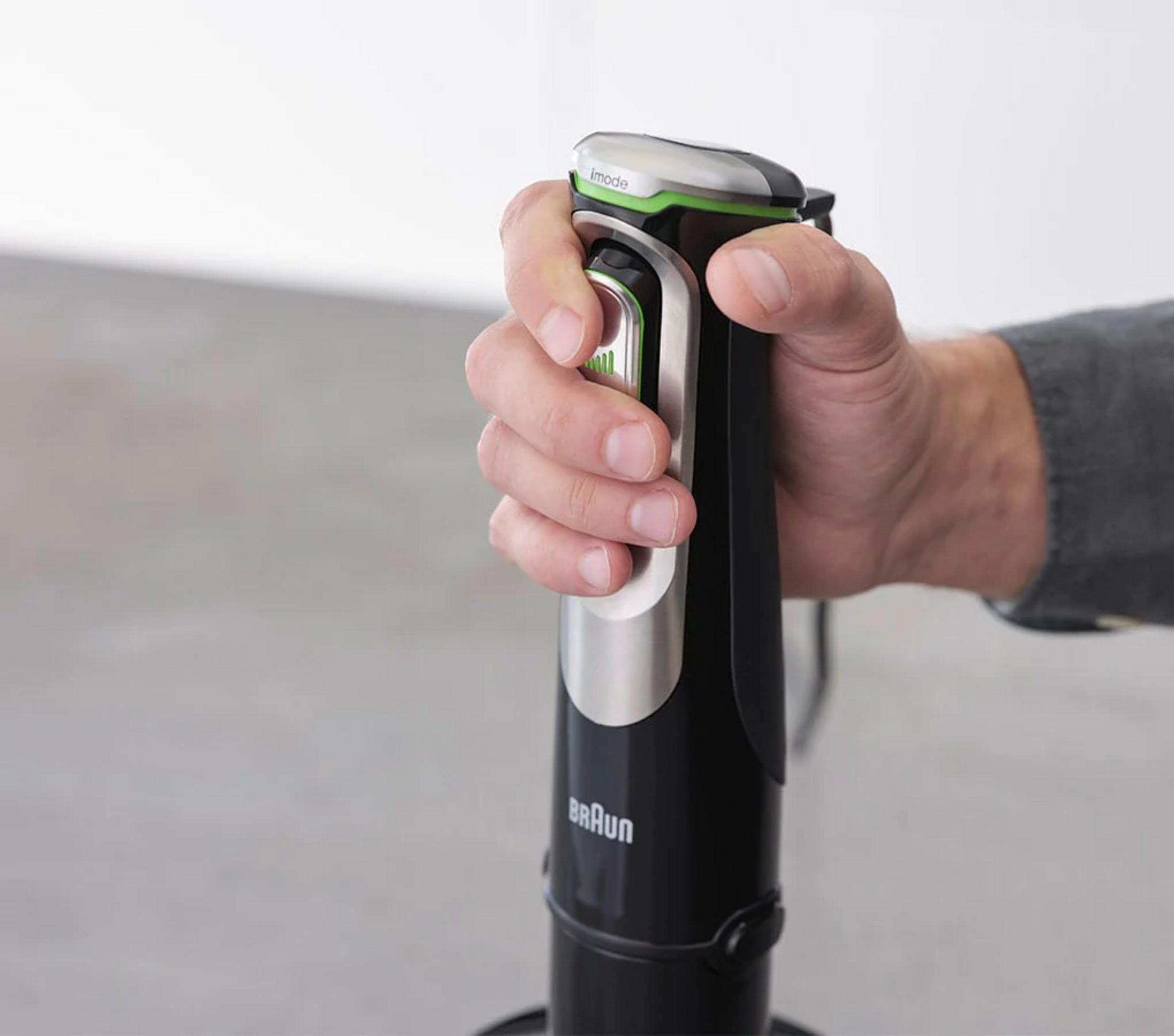 Een hand houdt een zwarte staafmixer vast met zilveren en groene accenten.