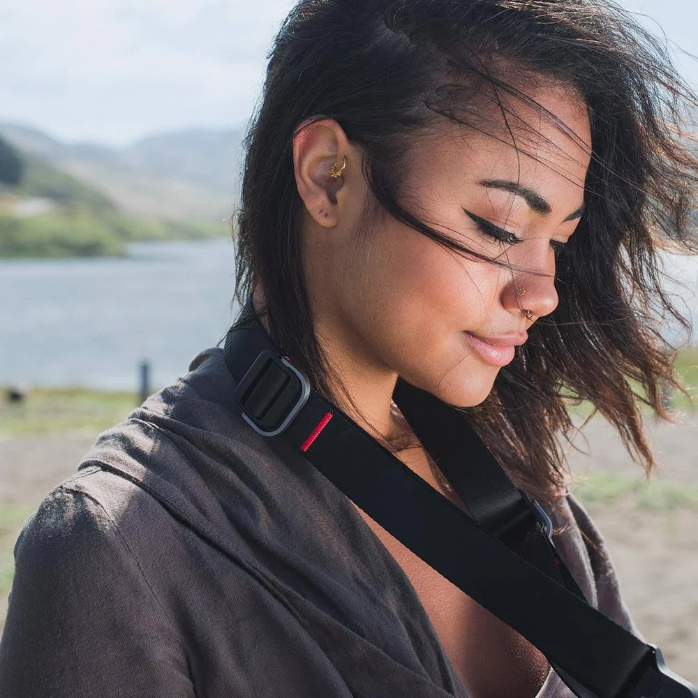 Młoda kobieta z paskiem aparatu na zewnątrz nad jeziorem.