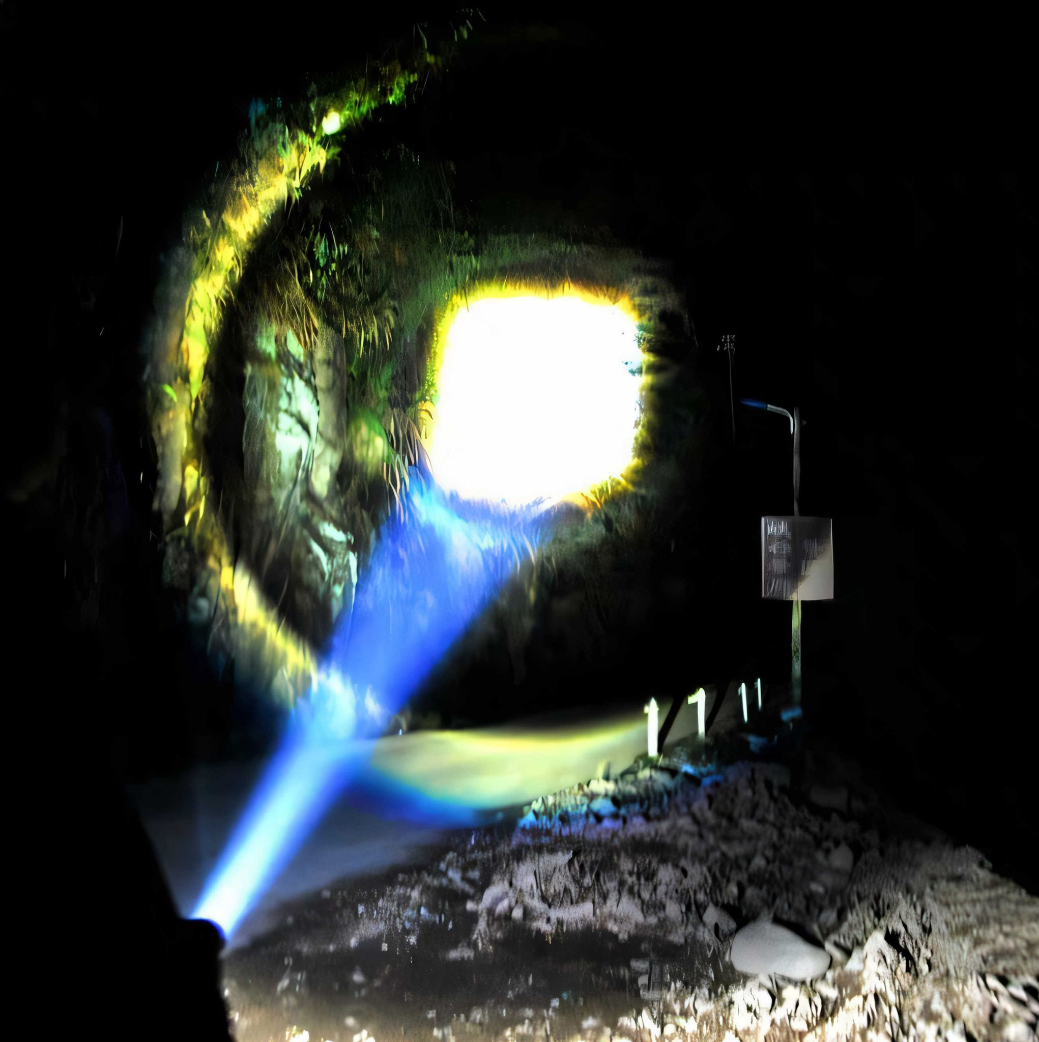 Taschenlampe beleuchtet Höhlenwand mit blauem Lichtstrahl und gelben Reflexen.