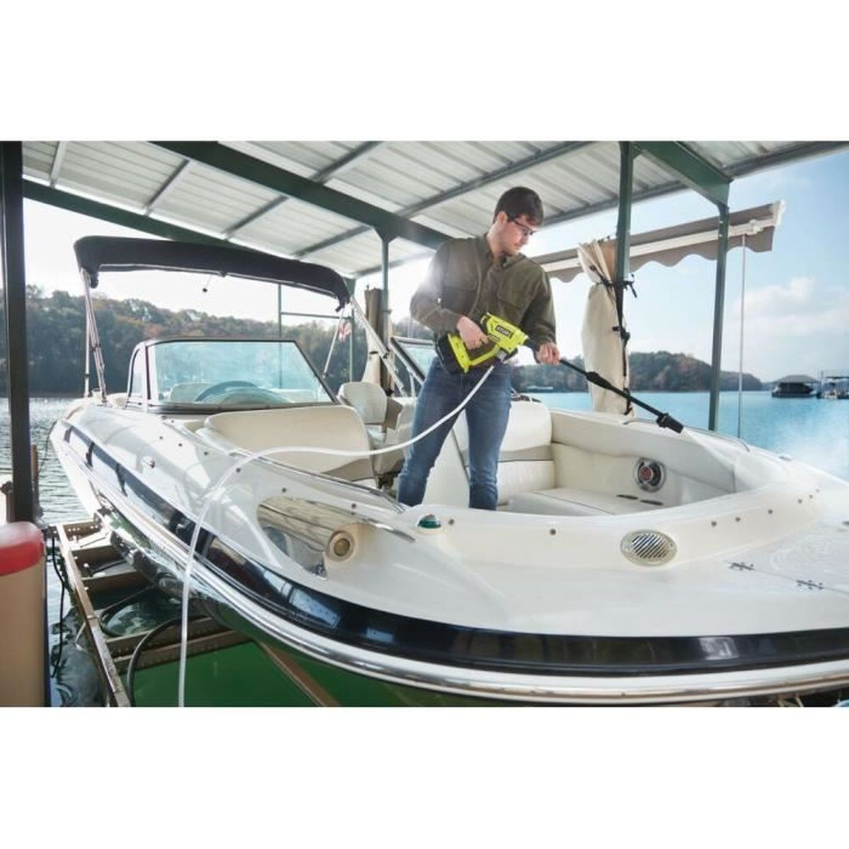 Ein Mann reinigt ein Boot mit einem Hochdruckreiniger unter einem Vordach am Wasser.