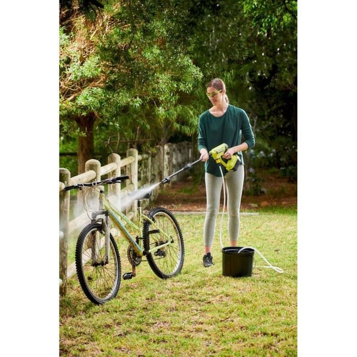 Eine Frau reinigt ein Fahrrad mit einem Hochdruckreiniger im Freien.
