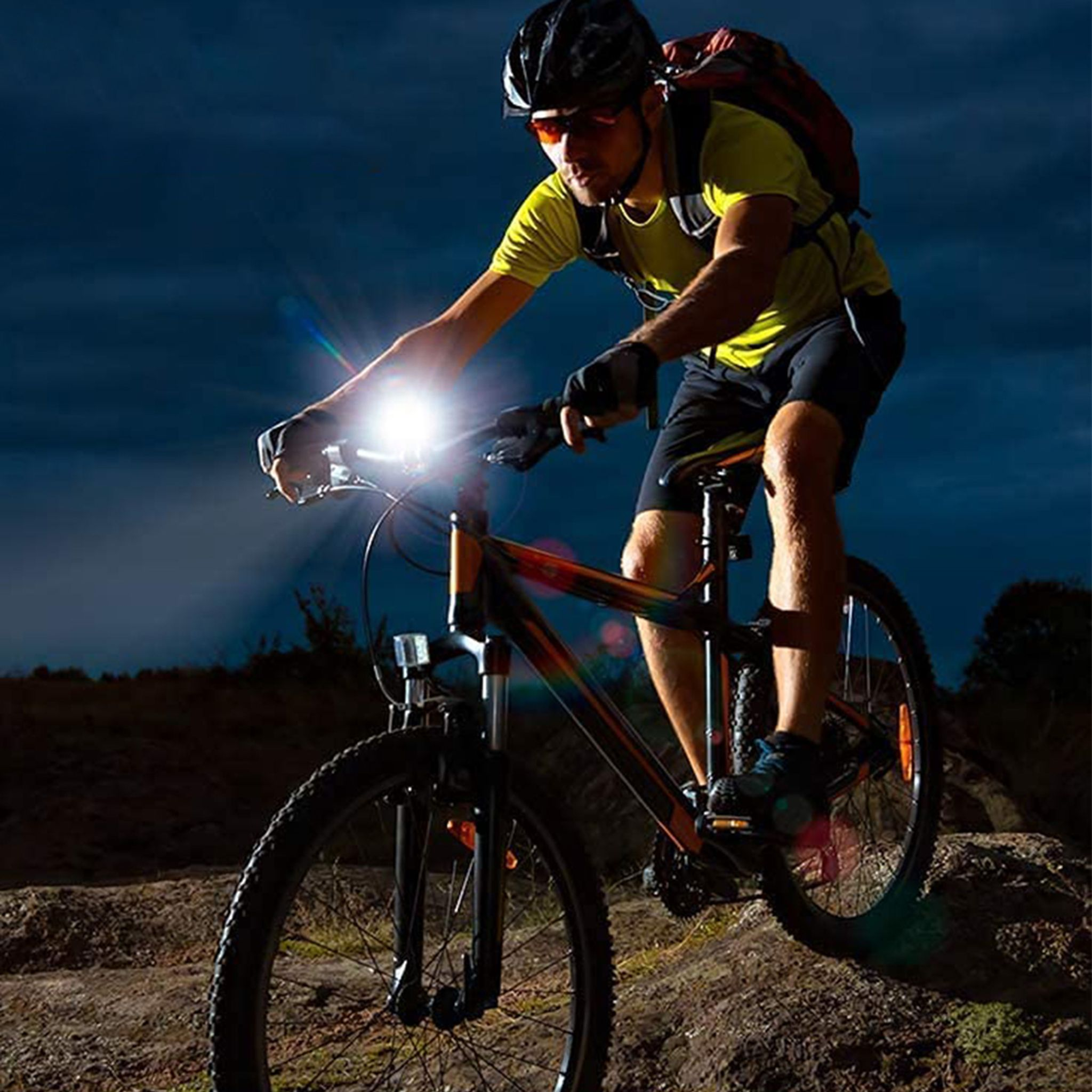 Mann fährt nachts Mountainbike, beleuchtet von hellem Scheinwerfer.