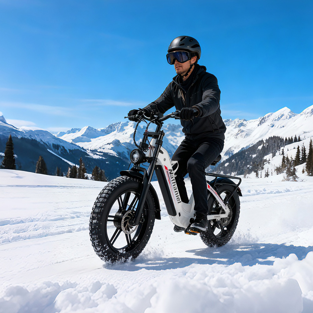 Mann fährt E-Bike im Schnee mit Berggipfeln im Hintergrund.